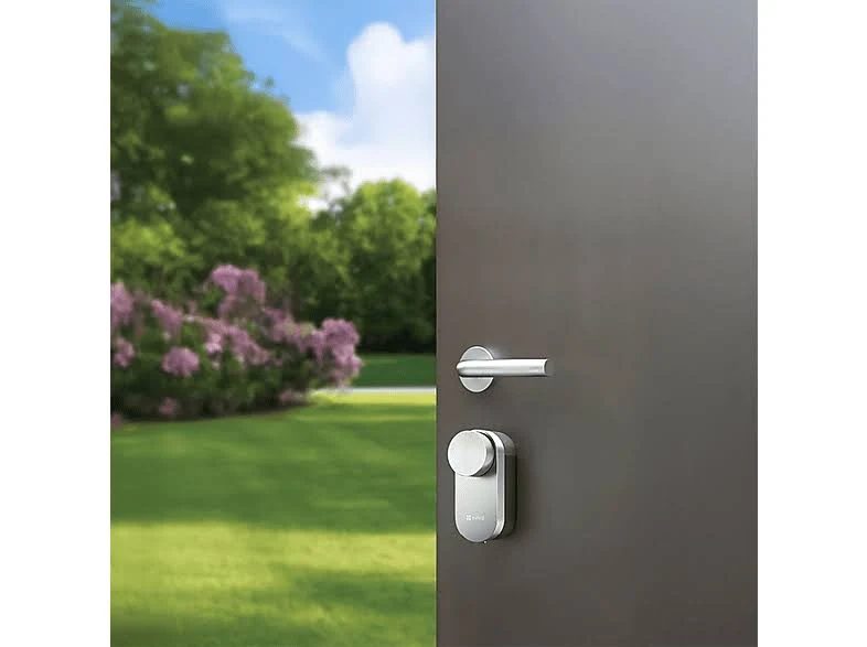 Una puerta con manija y cerradura de metal está abierta. El fondo muestra un césped verde, árboles y flores moradas bajo un cielo azul.