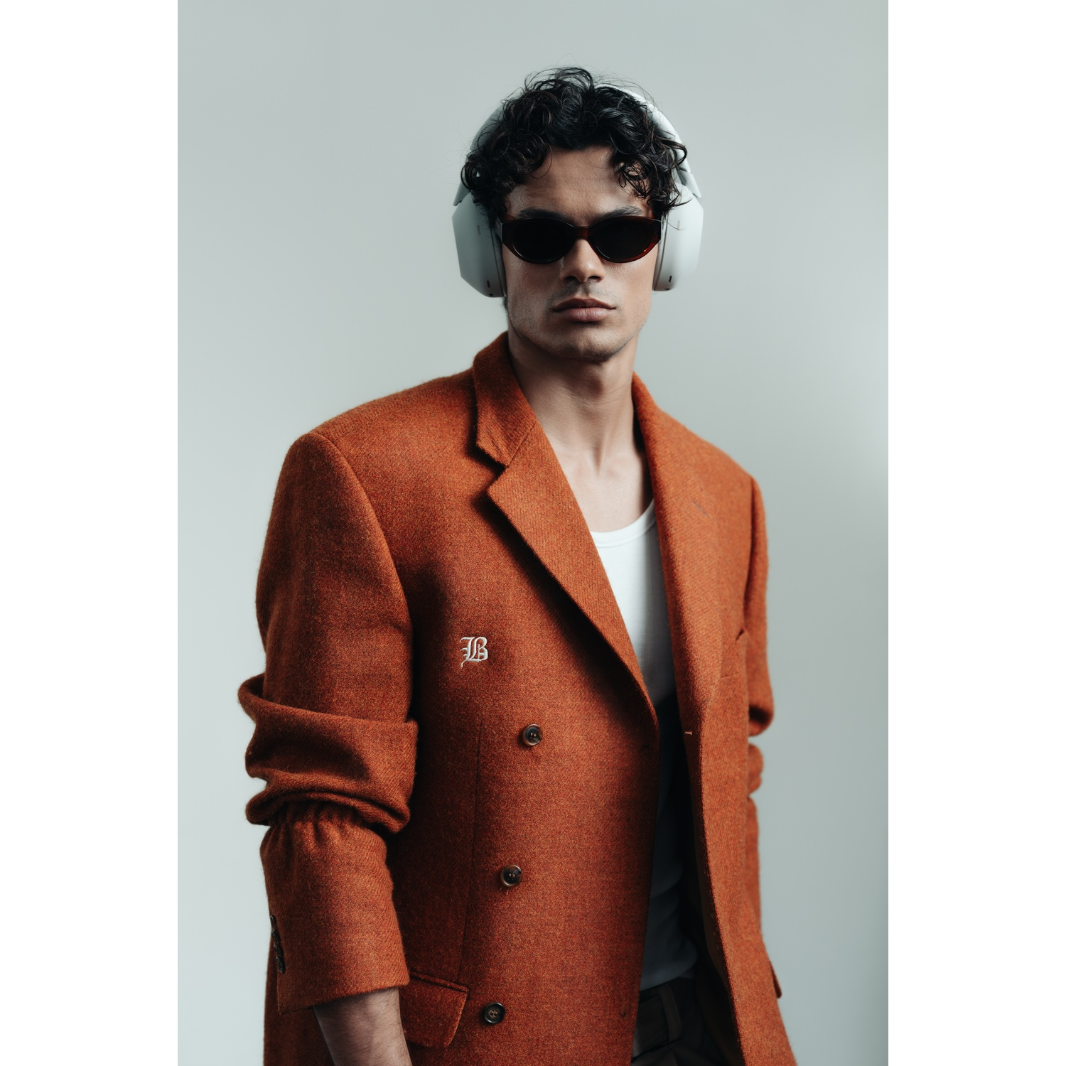 Un homme en blazer orange, lunettes de soleil et casque. Fond blanc. Il regarde la caméra.