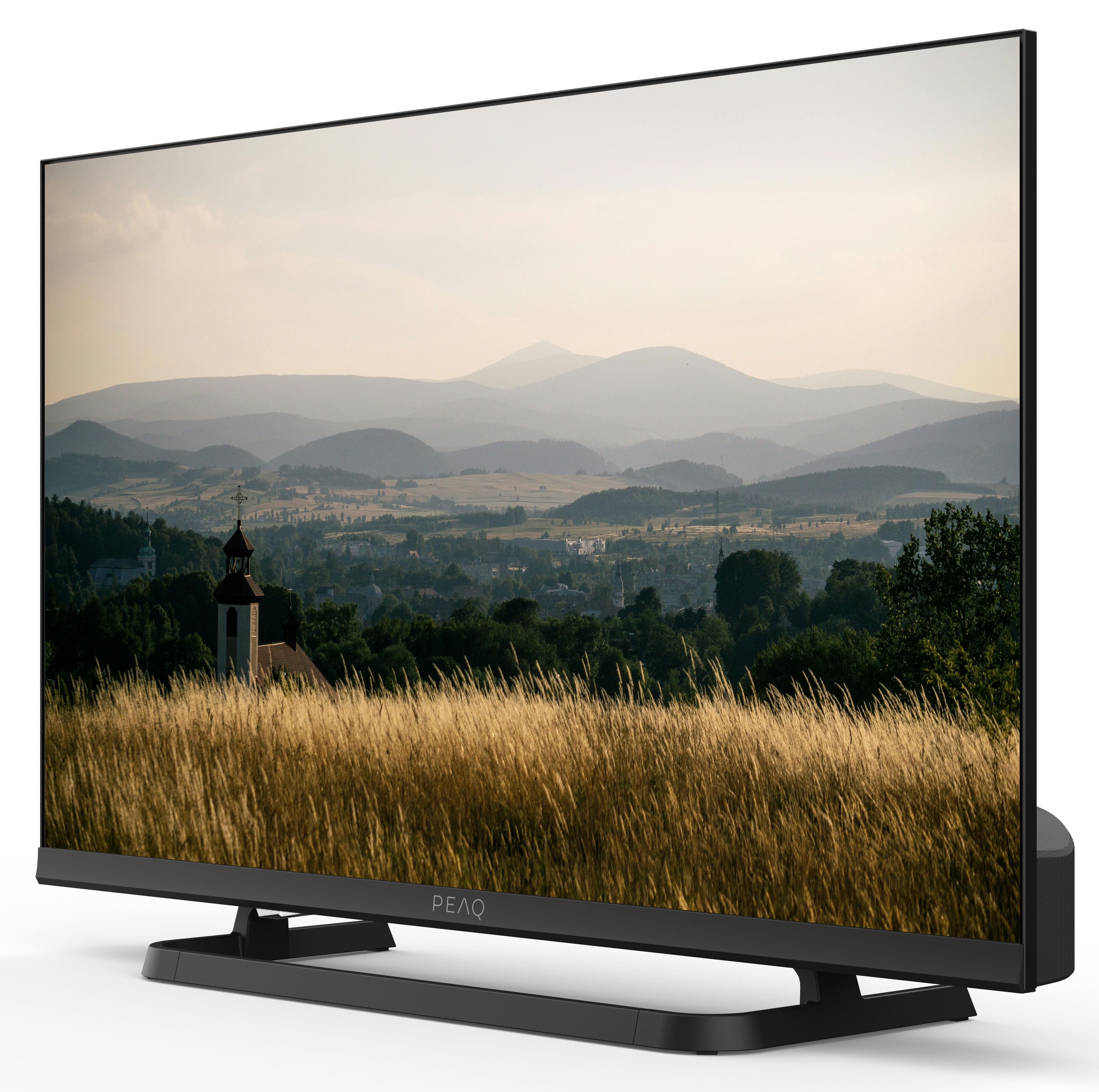 Telewizor wyświetla krajobraz z polami, górami i kościołem. Telewizor jest czarny z czarną podstawą.