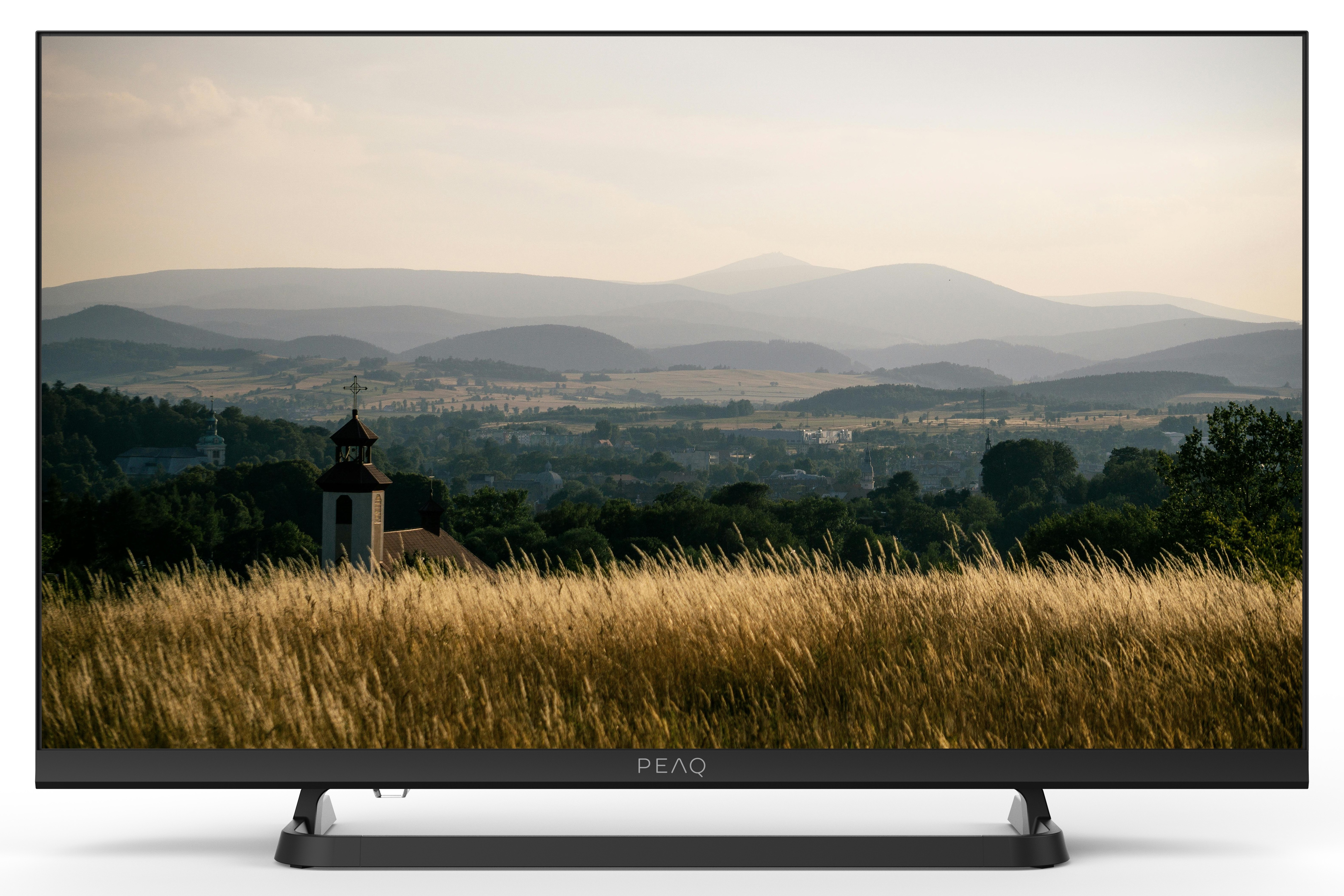 Scena krajobrazowa na ekranie telewizora. Widoczne góry i wioska. Wysoka trawa na pierwszym planie.