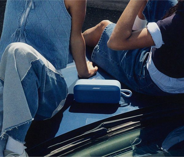 Dwie osoby siedzą na samochodzie, niebieski głośnik na masce. Mają na sobie dżinsy. Samochód jest niebieski.