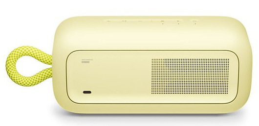 Jasnożółty głośnik z limonkowym uchwytem z liny. Ma siatkę otworów i port USB-C. Głośnik stoi na białej powierzchni.
