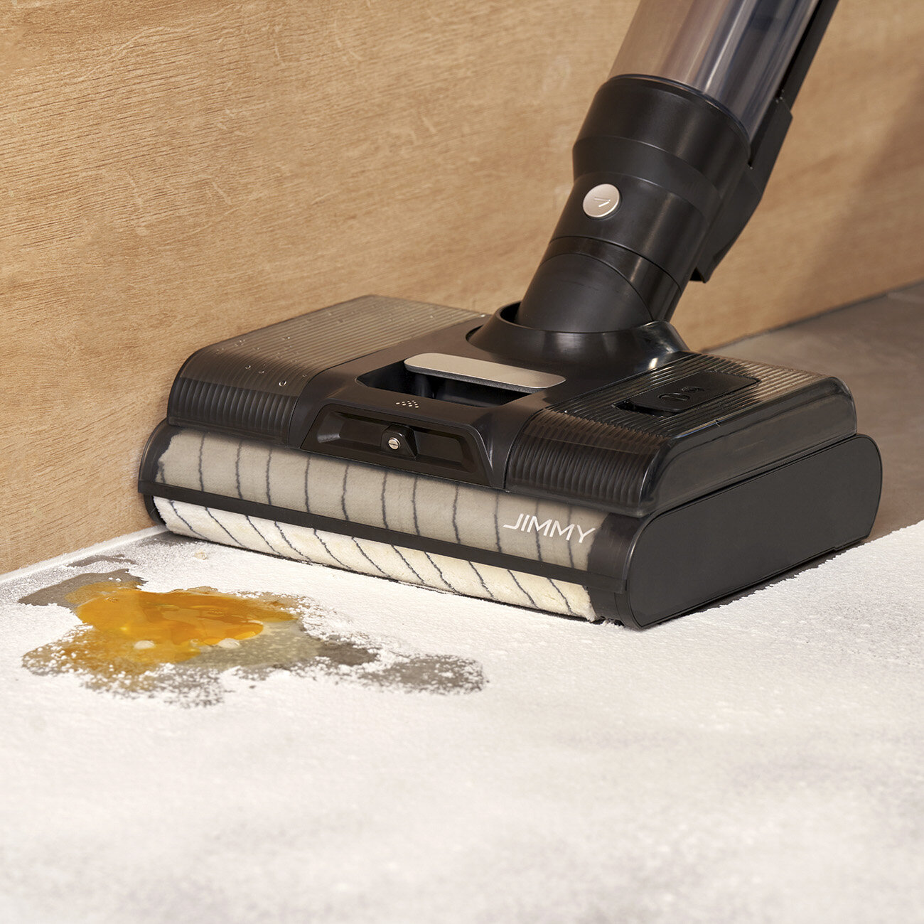 Czarny i srebrny odkurzacz czyści rozlaną ciecz. Rozlany płyn jest żółty, na białej podłodze.