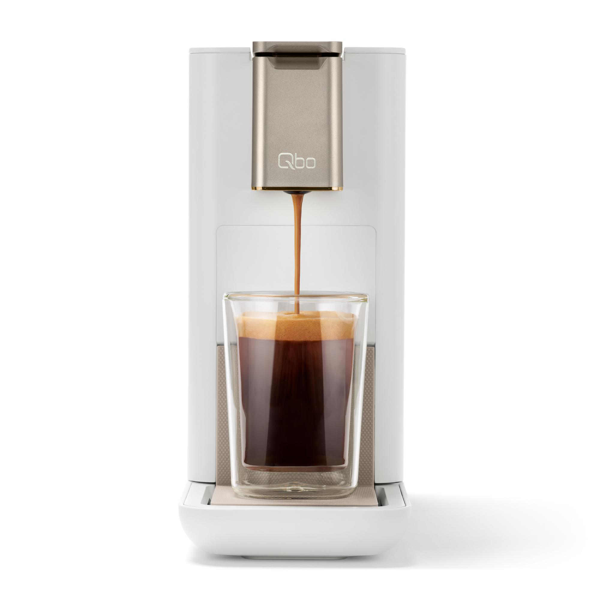Eine weiße Kaffeemaschine gibt Kaffee in ein Glas ab. Der Kaffee ist dunkel mit Schaum oben drauf.