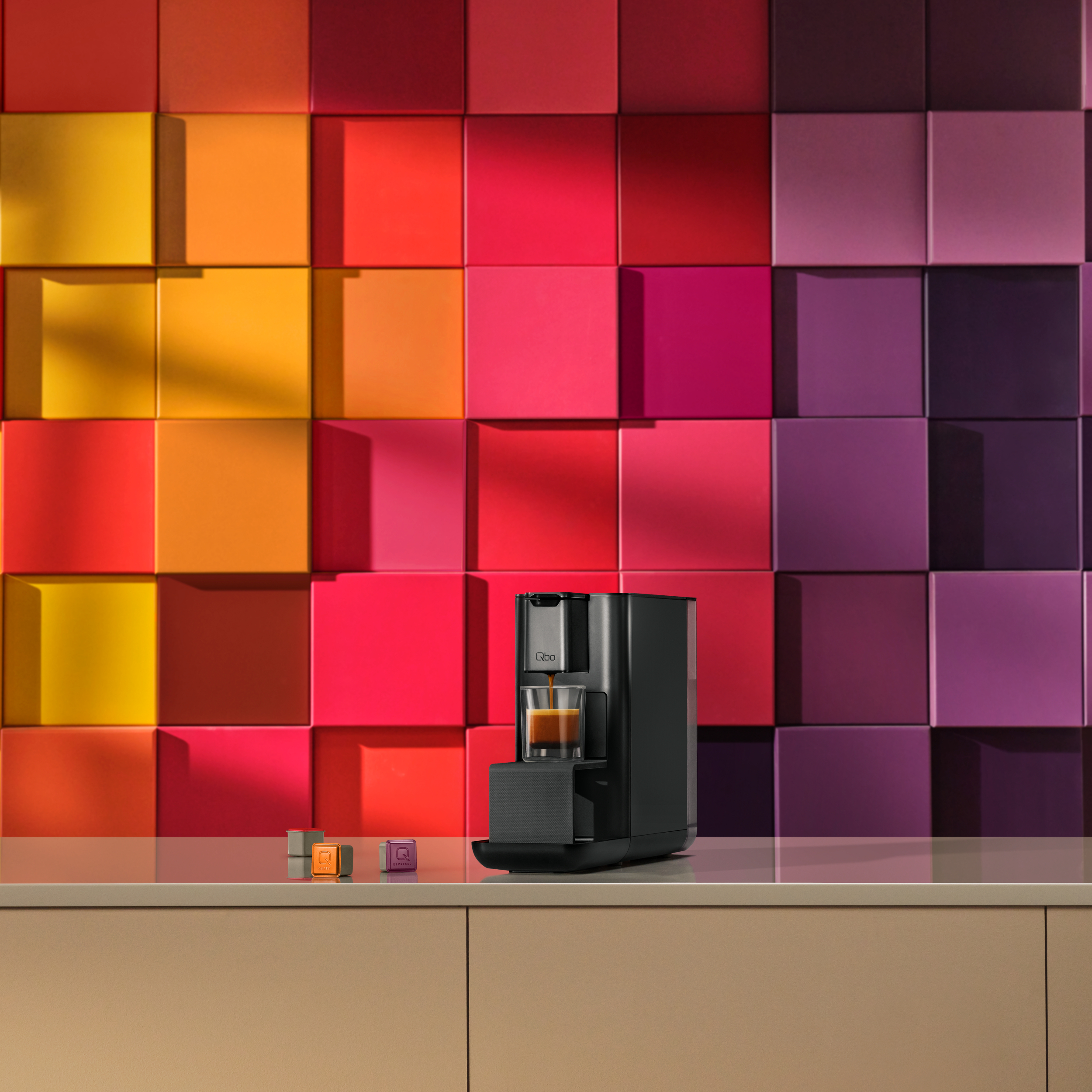 Eine schwarze Espressomaschine mit einem Schuss Kaffee. Bunter quadratischer Hintergrund. Drei Kaffeekapseln auf der Theke.