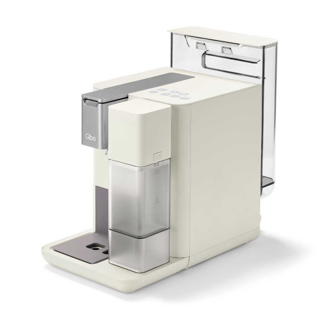 Cremefarbene Qbo-Kaffeemaschine mit Wassertank, Silberelement und grauer Tropfschale, vor weißem Hintergrund.