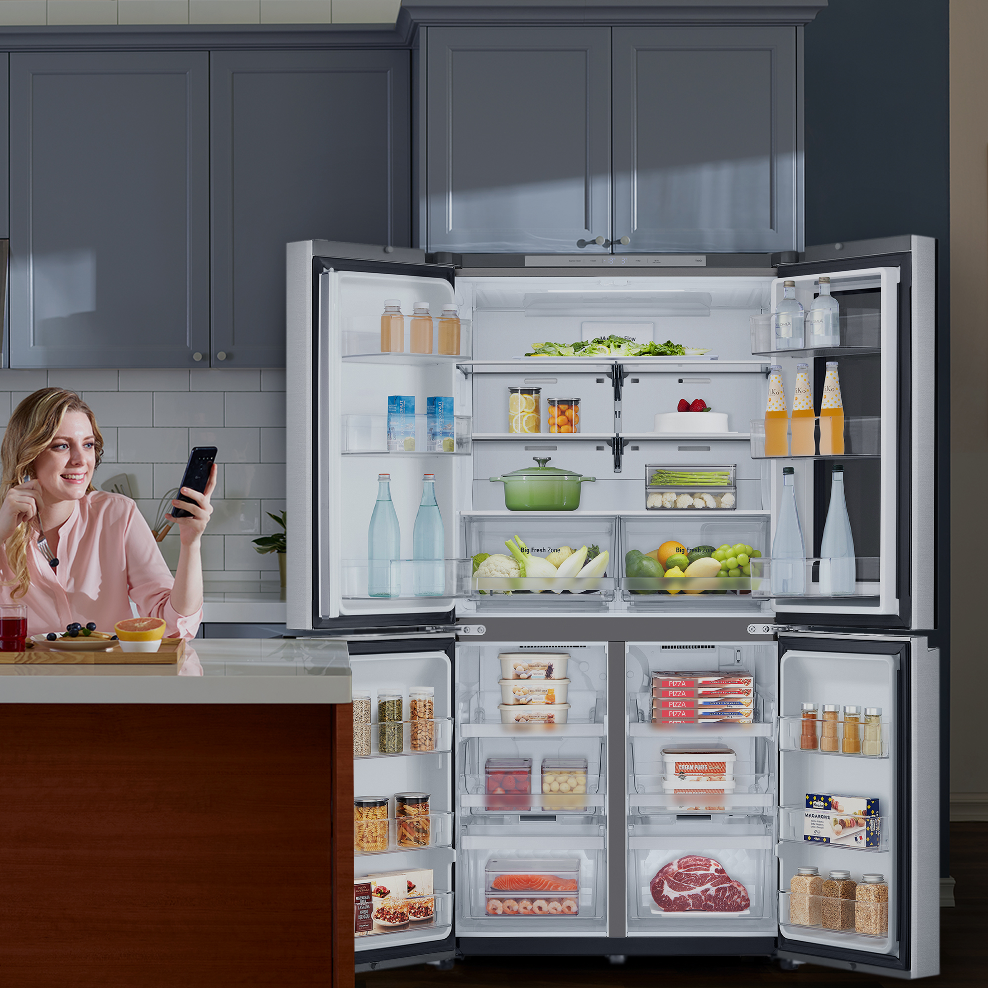 Mujer con teléfono cerca de la nevera abierta. La nevera tiene alimentos como frutas, verduras y bebidas.