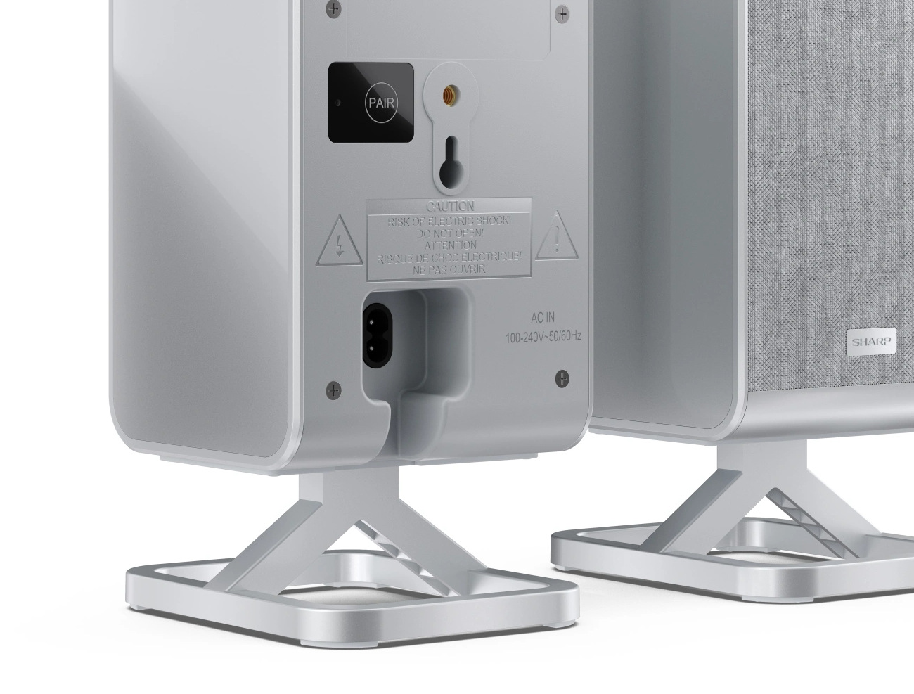 Dwa białe głośniki ze srebrnymi podstawkami. Jeden ma materiałowy przód, drugi tył z ostrzeżeniami i wejściem zasilania.