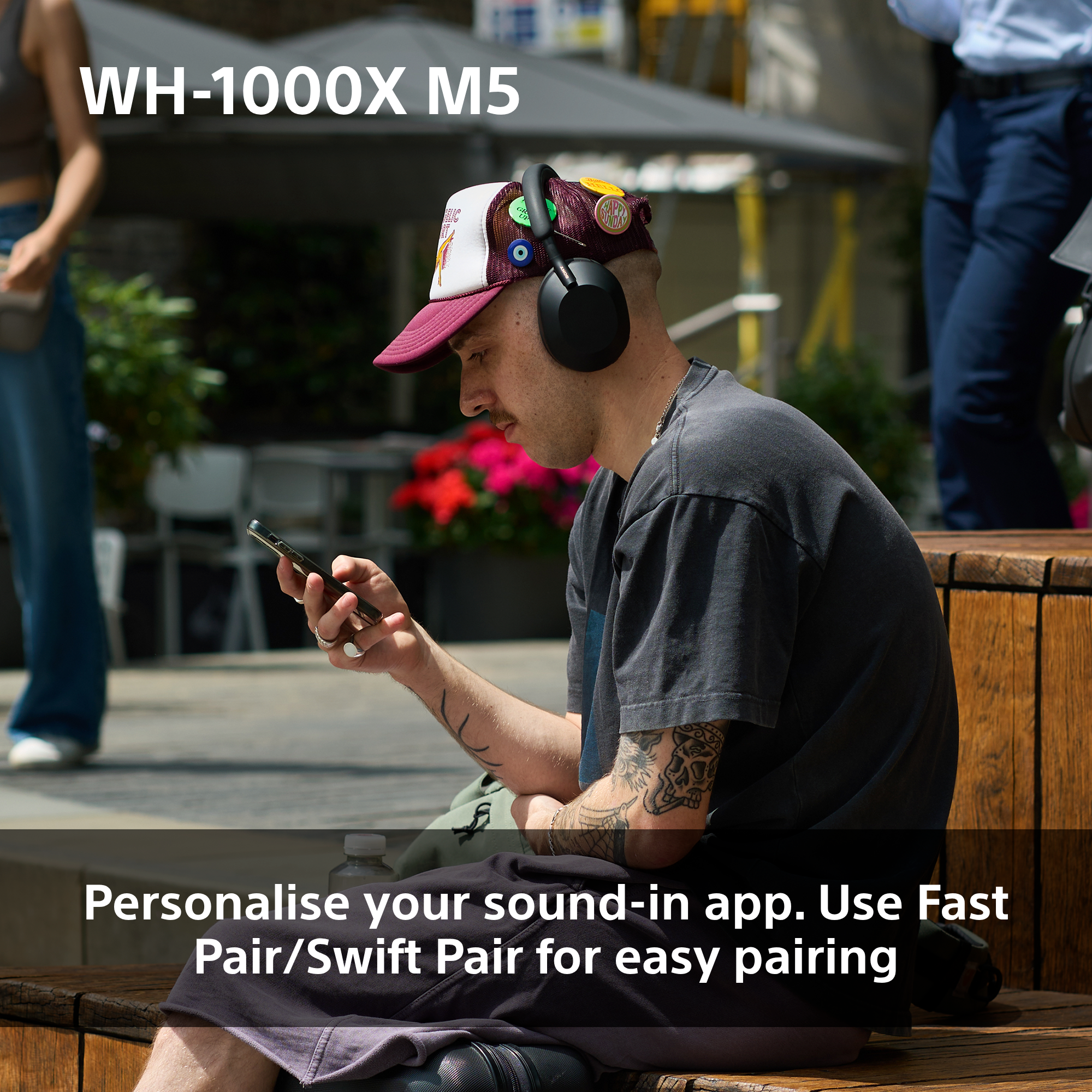 Ein Mann mit Kopfhörern, Mütze und Tätowierungen hält ein Telefon. Der Text lautet 'Personalisiere deinen Sound'.