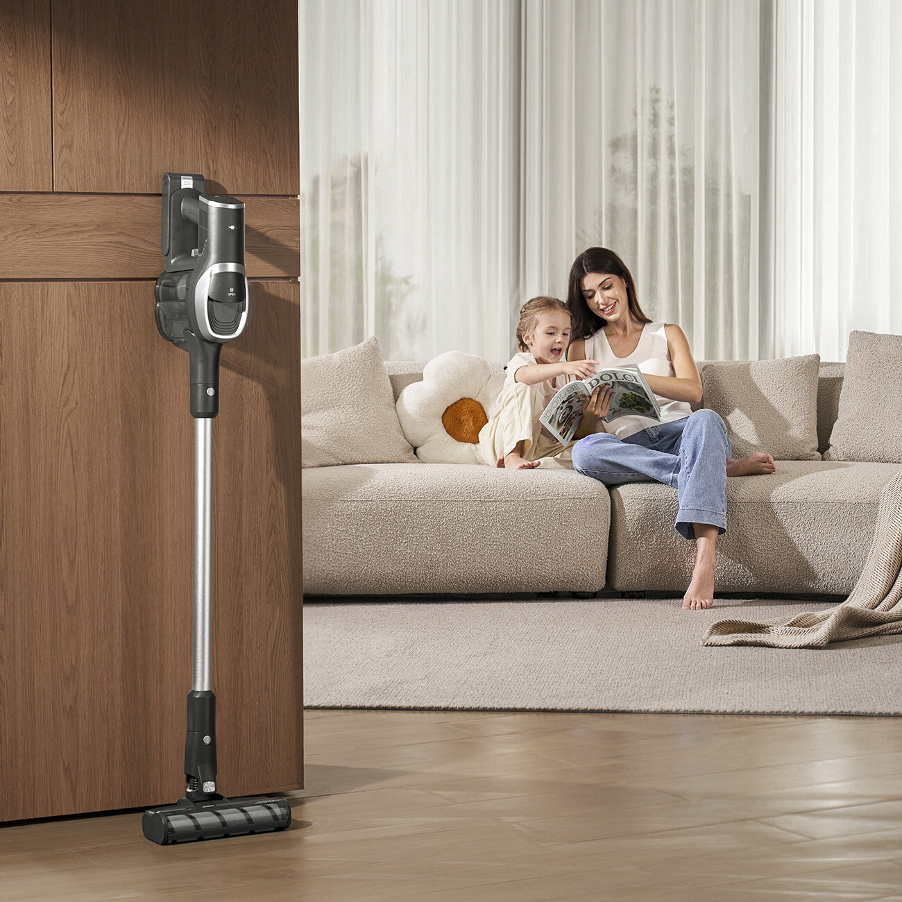 Kobieta i dziecko czytają na kanapie. Odkurzacz stoi przy drewnianych drzwiach. Na kanapie jest poduszka w kształcie kwiatu.