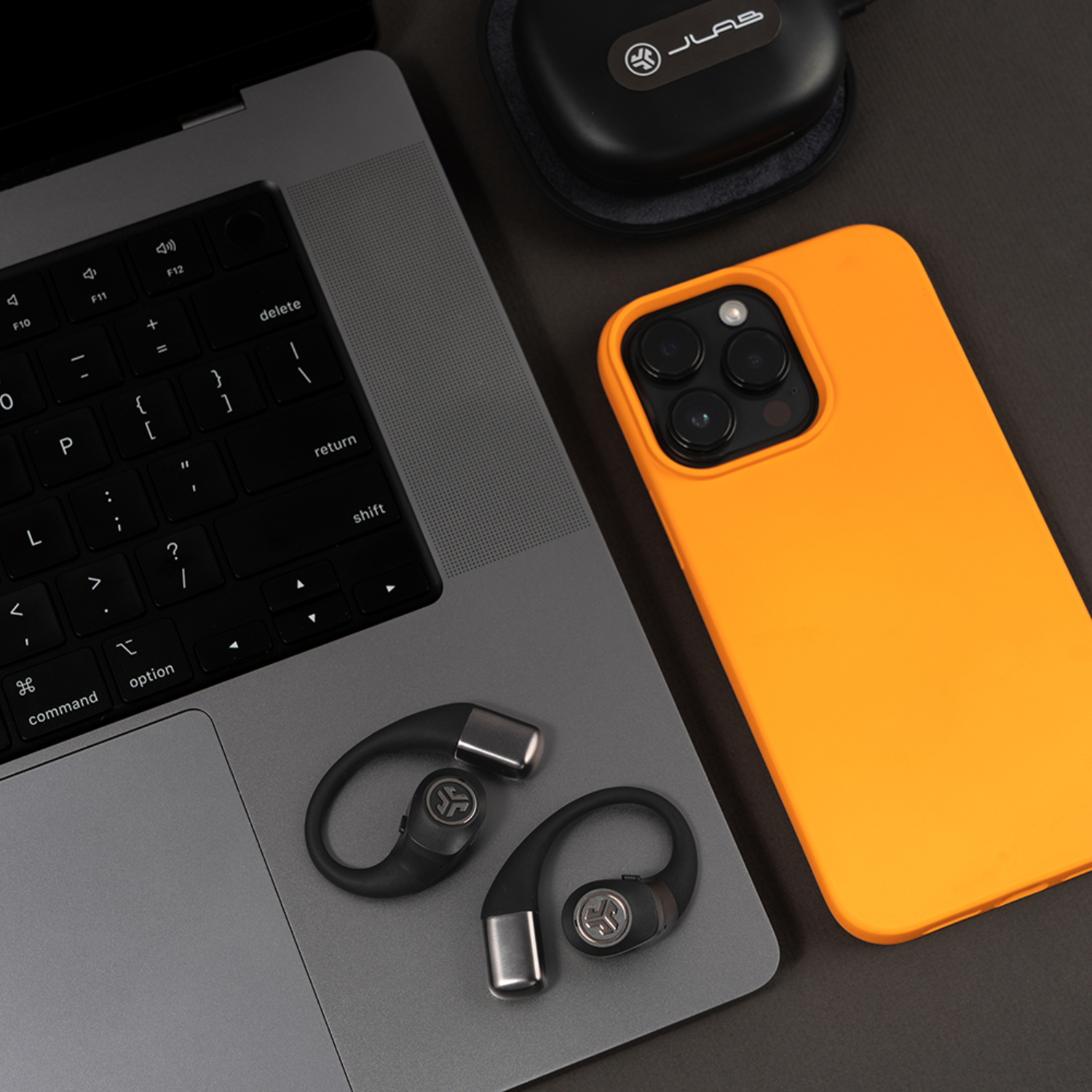 Un ordinateur portable, un téléphone orange, des écouteurs noirs et un étui noir sont sur une surface sombre. Les écouteurs sont près du clavier de l'ordinateur portable.