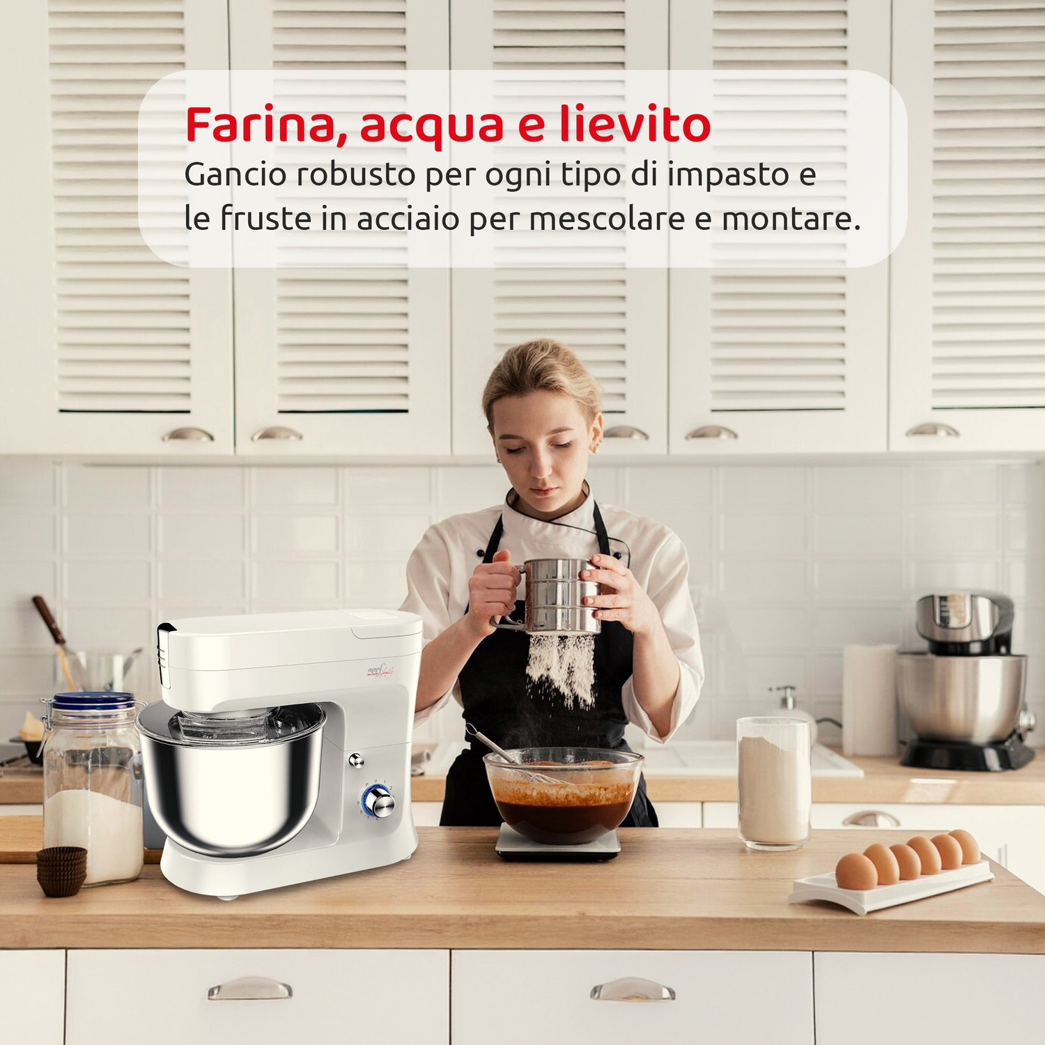 Una donna setaccia la farina in una ciotola. Un mixer bianco e gli ingredienti sono su un bancone di legno in una cucina. Uova a lato.