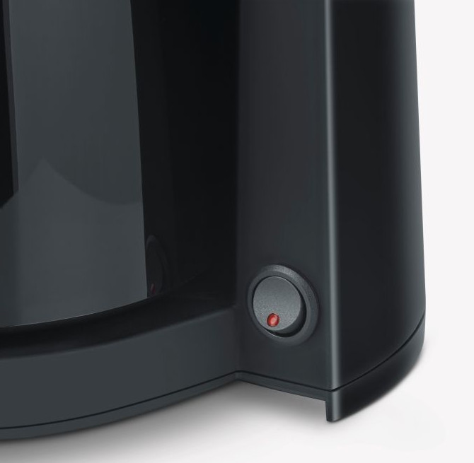 Zbliżenie ciemnoszarego ekspresu do kawy z okrągłym przyciskiem zasilania. Przycisk jest włączony i podświetlony czerwonym światłem.