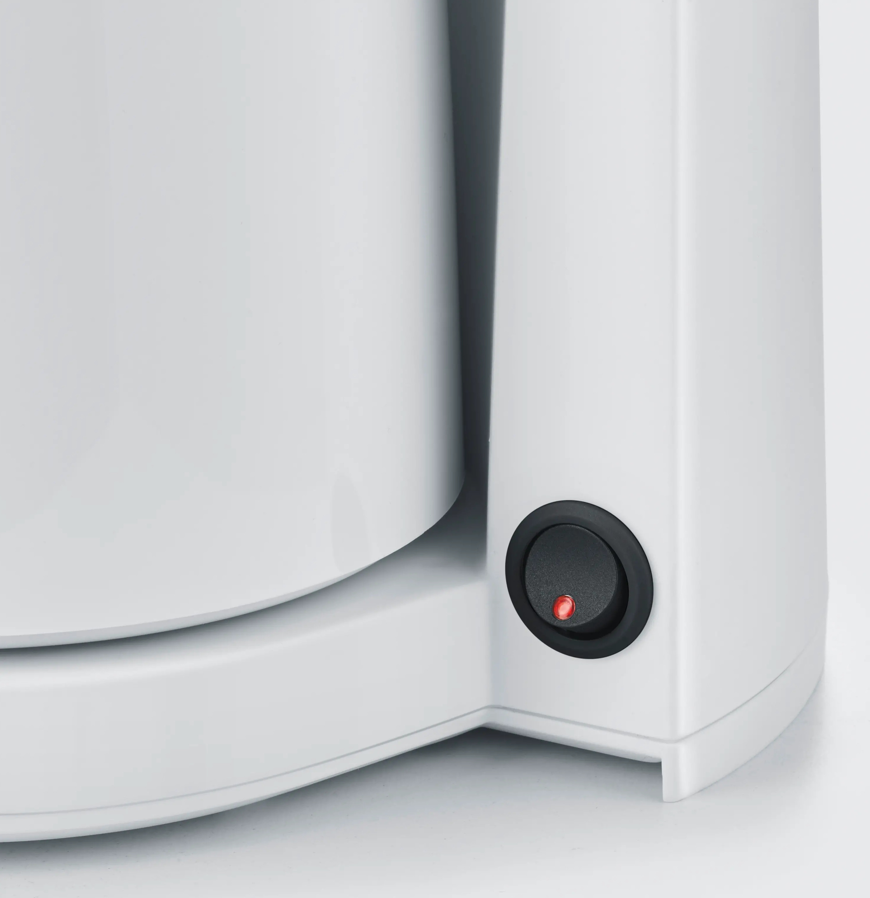 Zbliżenie białego urządzenia. Widoczny jest czarny przycisk zasilania z czerwoną lampką. Tło jest białe.
