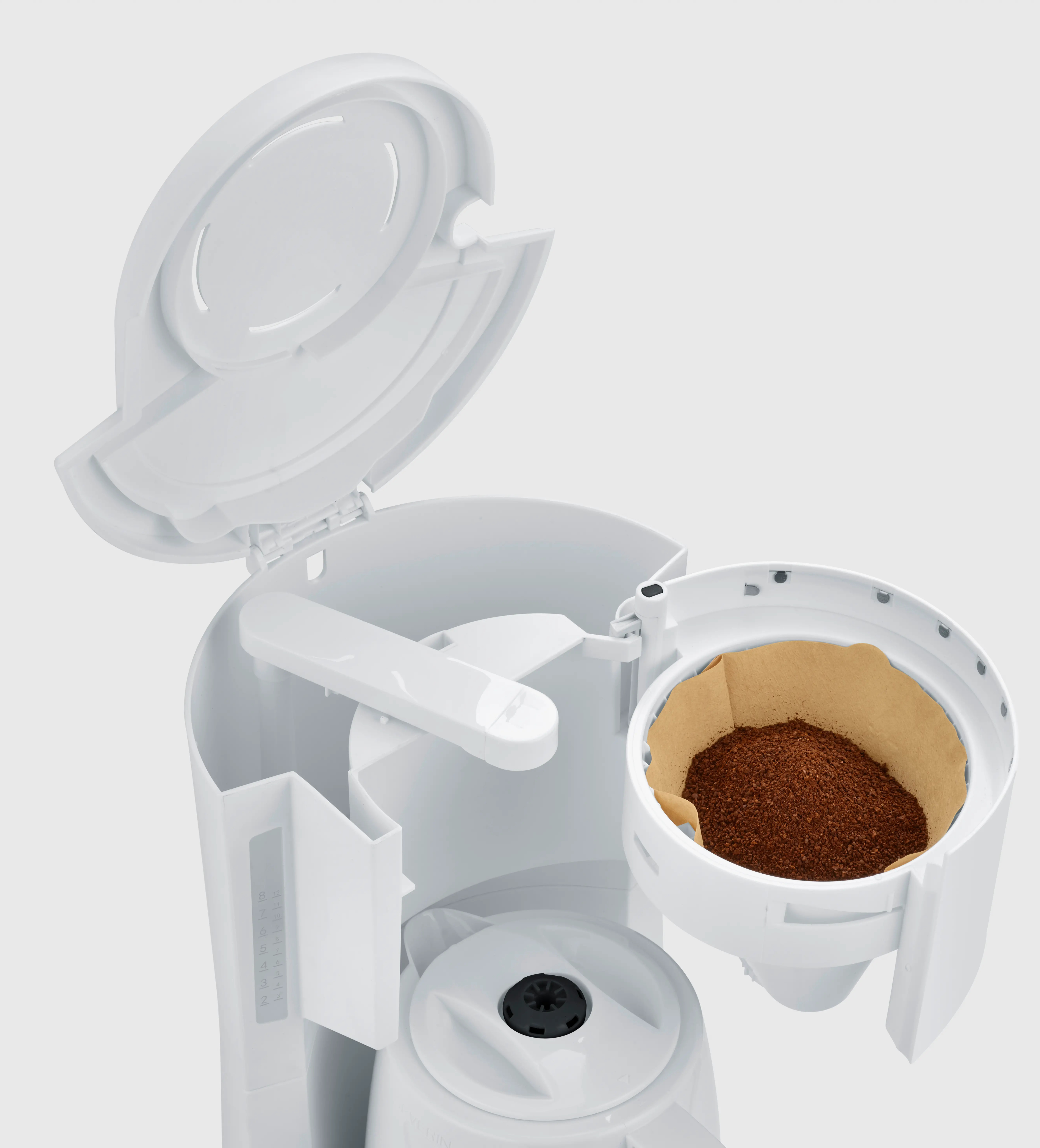 Biały ekspres do kawy z otwartą pokrywą. Brązowy filtr do kawy z mieloną kawą w środku. Tło jest białe.