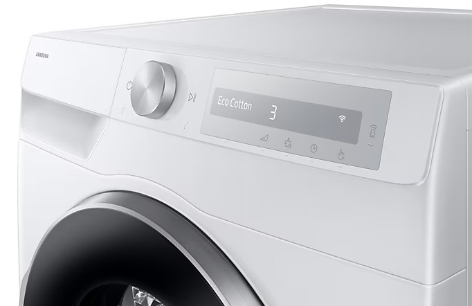 Zbliżenie panelu sterowania białej pralki Samsung. Ma pokrętło, wyświetlacz z napisem 'Eco Cotton 3' i różne ikony.