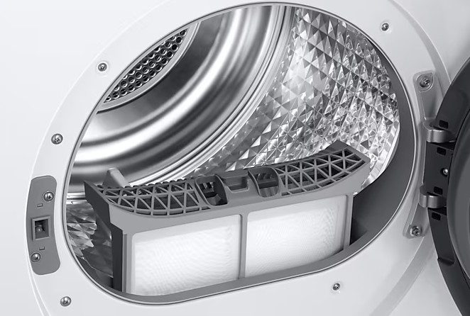 Wewnątrz suszarki. Filtr, szary plastik, znajduje się w bębnie ze stali nierdzewnej. Drzwi są otwarte.