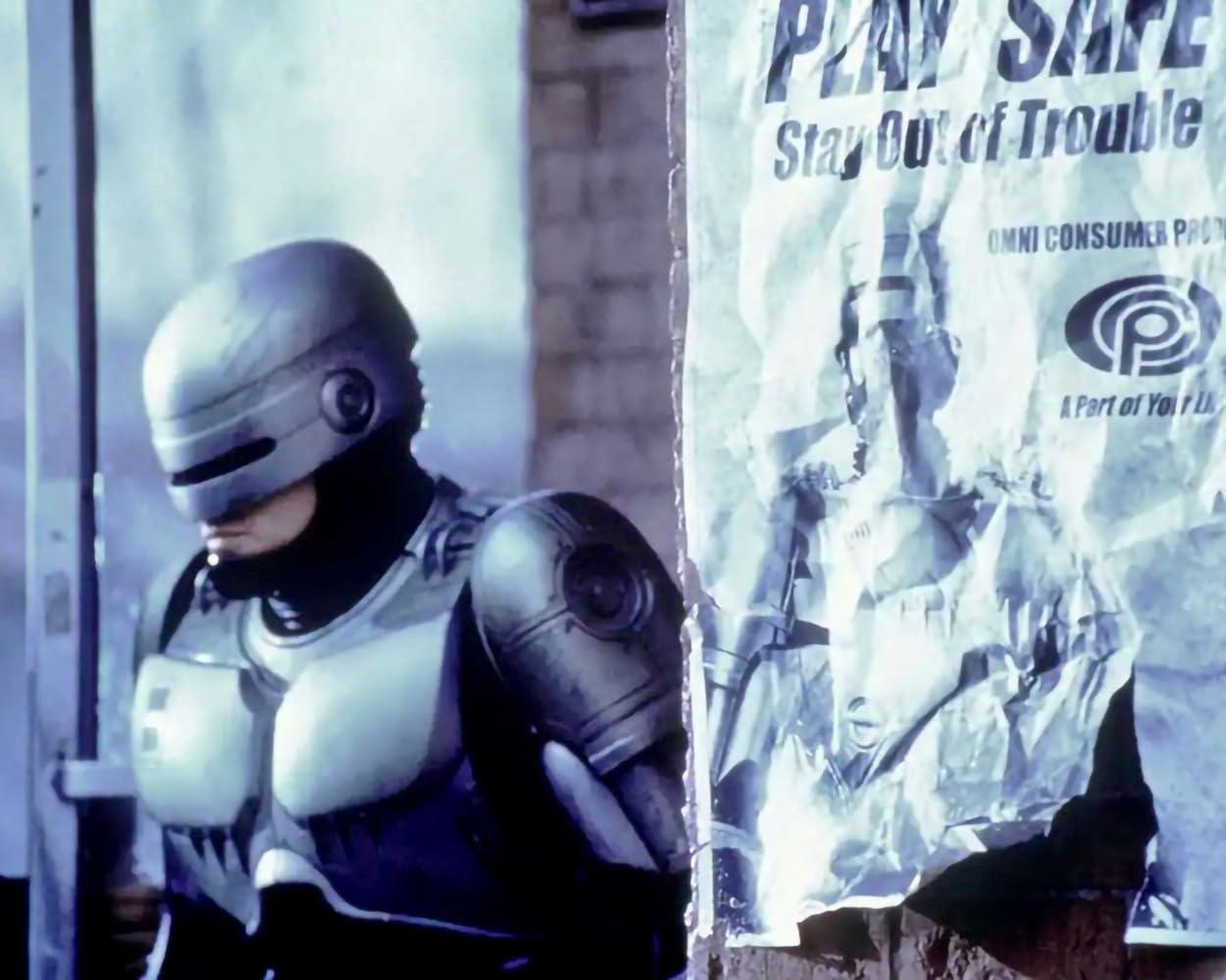 RoboCop steht in der Nähe eines Plakats. Das Plakat lautet: 'Play Safe, Stay Out of Trouble'. Er trägt einen metallischen Helm und eine Rüstung.