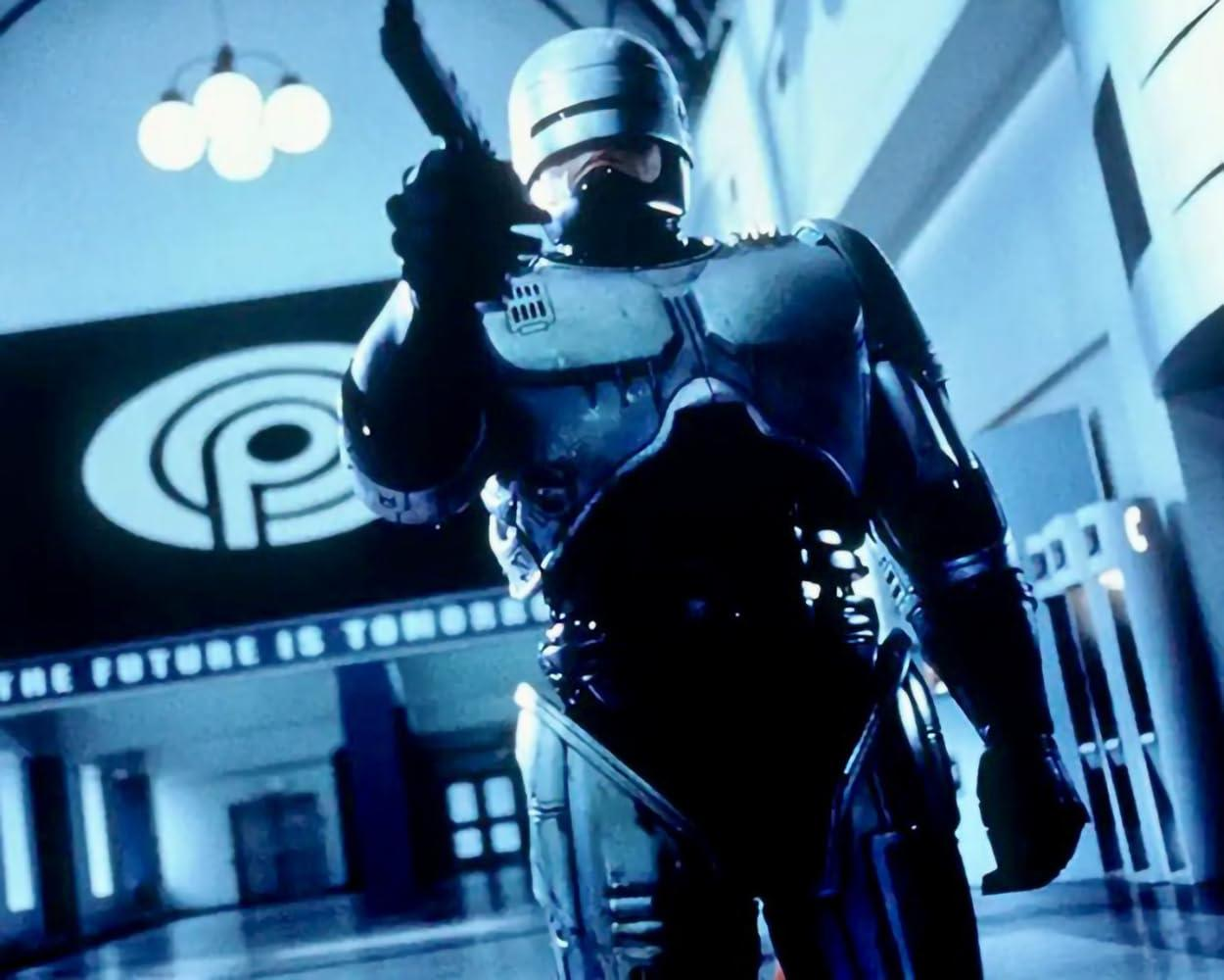 RoboCop, ein Cyborg-Polizist, zielt mit einer Waffe. Eine futuristische Szene mit Logo und Text im Hintergrund. Bläulich getöntes Bild.