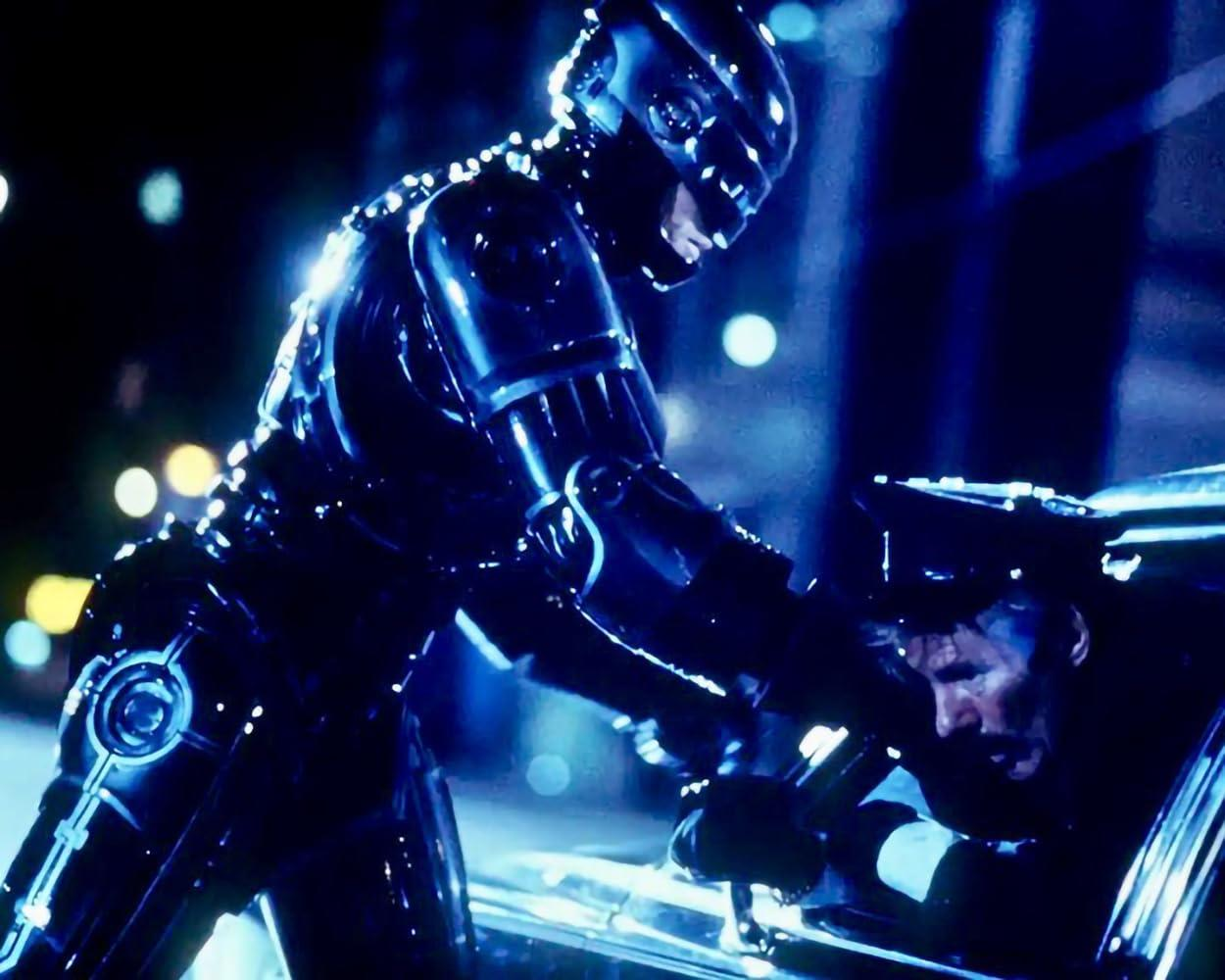 RoboCop verhaftet einen Mann in einem Auto. Die Szene ist dunkel mit blauen und gelben Lichtern. RoboCop trägt einen schwarzen Anzug.