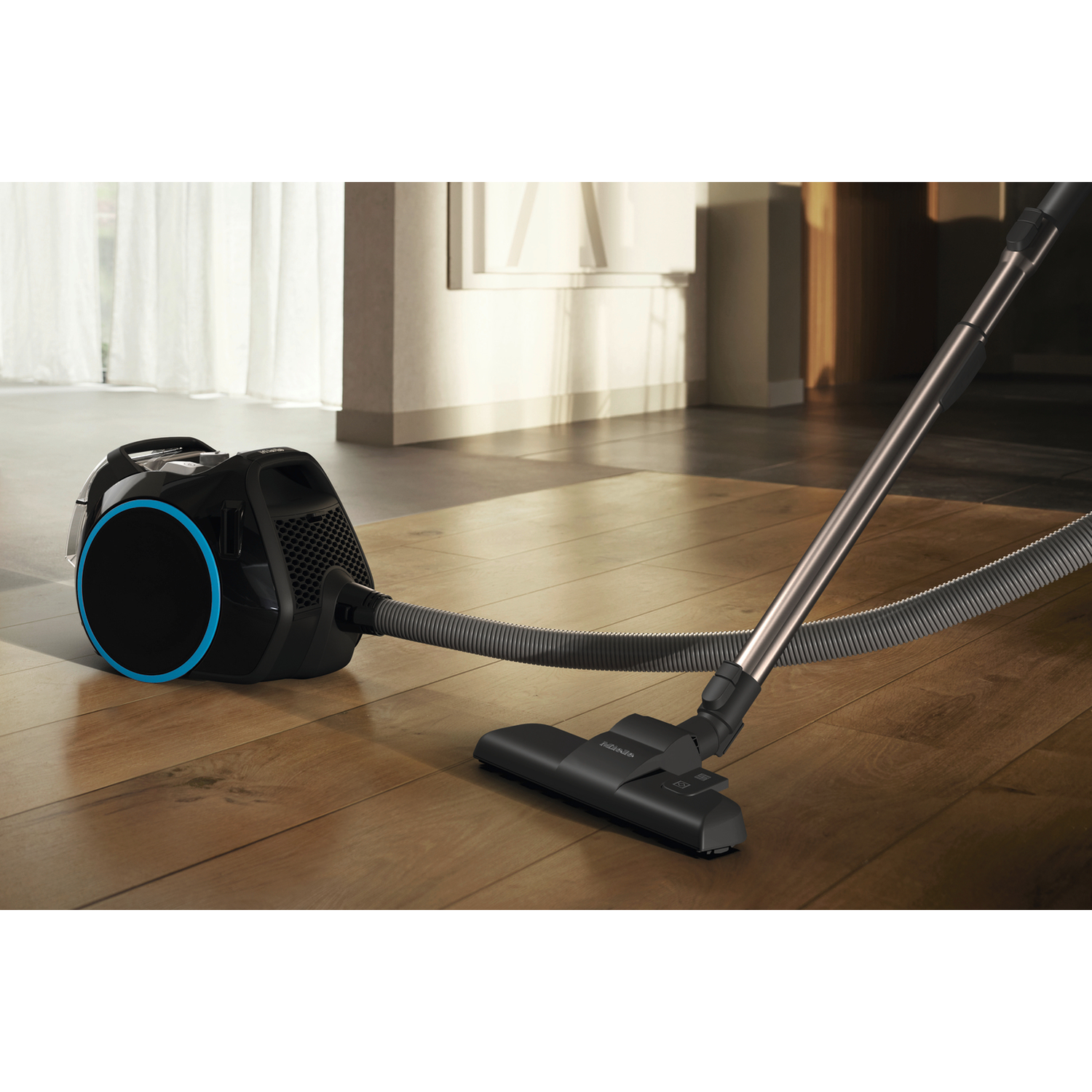 A black and blue vacuum cleaner on a wooden floor. The vacuum hose and head are visible. Background shows a door and window.
