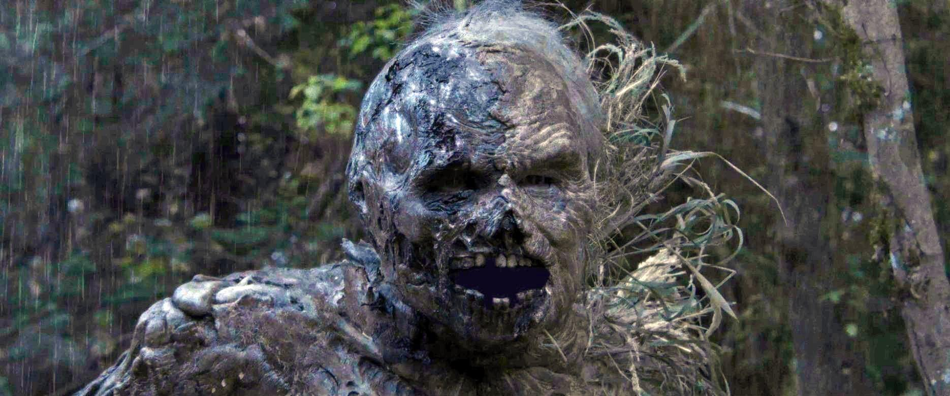 Eine zombieartige Kreatur mit offenem Mund steht in einem Wald. Es regnet, und die Kreatur hat graue Haut und freiliegende Zähne.