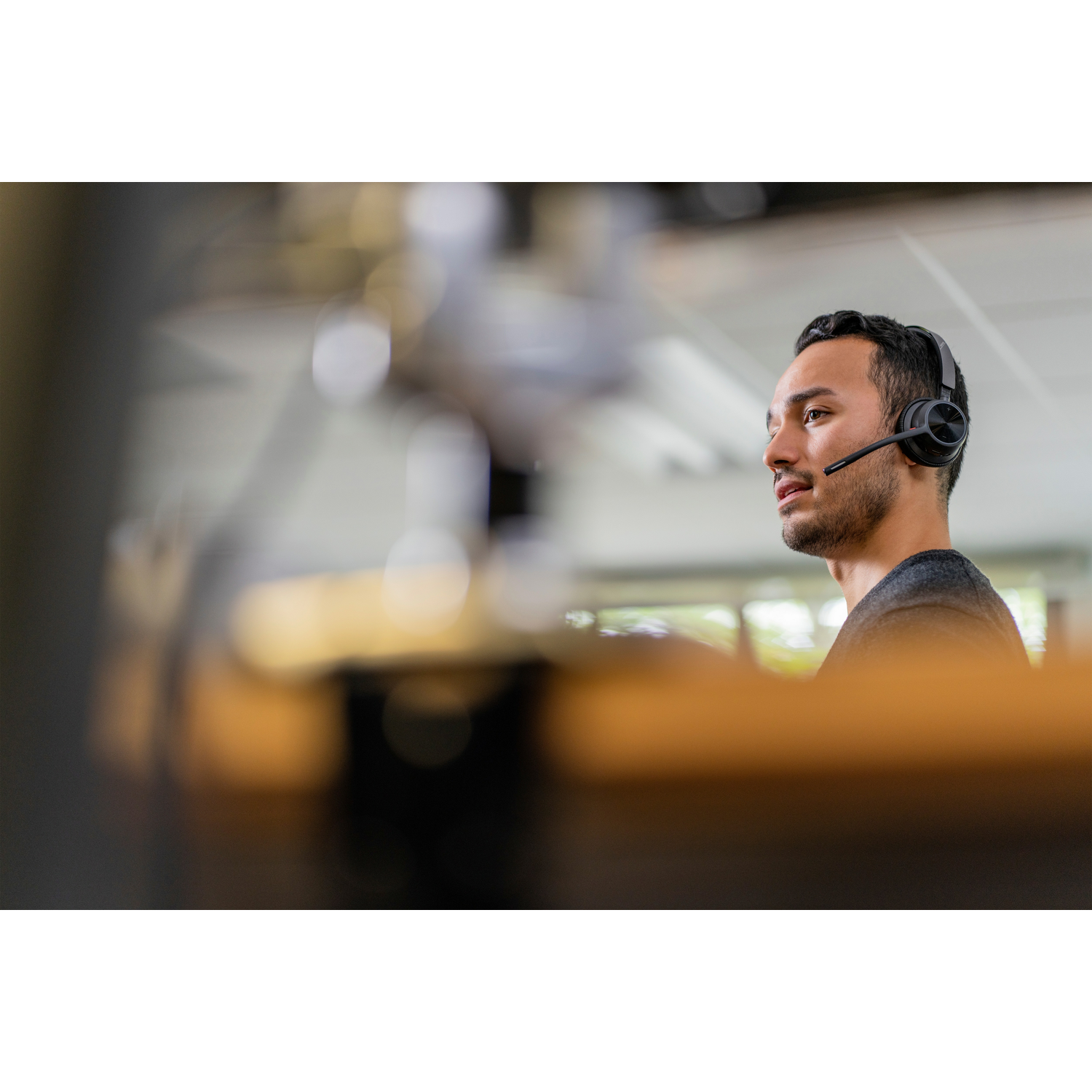 Een man met een headset kijkt naar rechts. De achtergrond is wazig en toont een kantooromgeving. Hij staat in profiel.