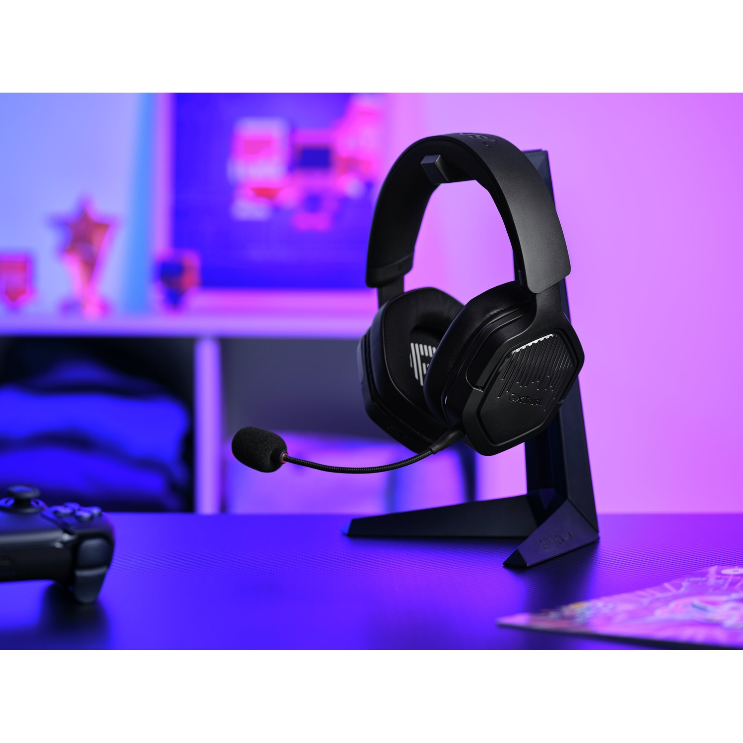 Cuffie da gioco nere su un supporto. Un controller è sul tavolo. Lo sfondo ha una mensola e un premio a stella.