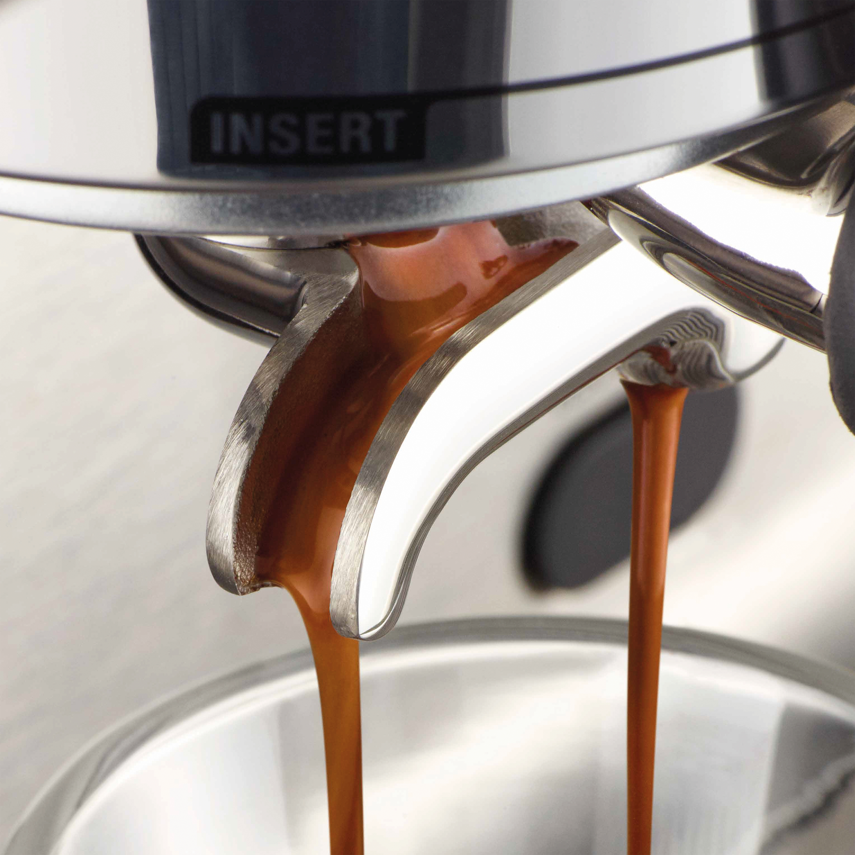 Espressomaschine, die Kaffee ausgibt. Dunkelbrauner Kaffee fließt aus dem Siebträger in ein Glas. Maschine ist metallisch.