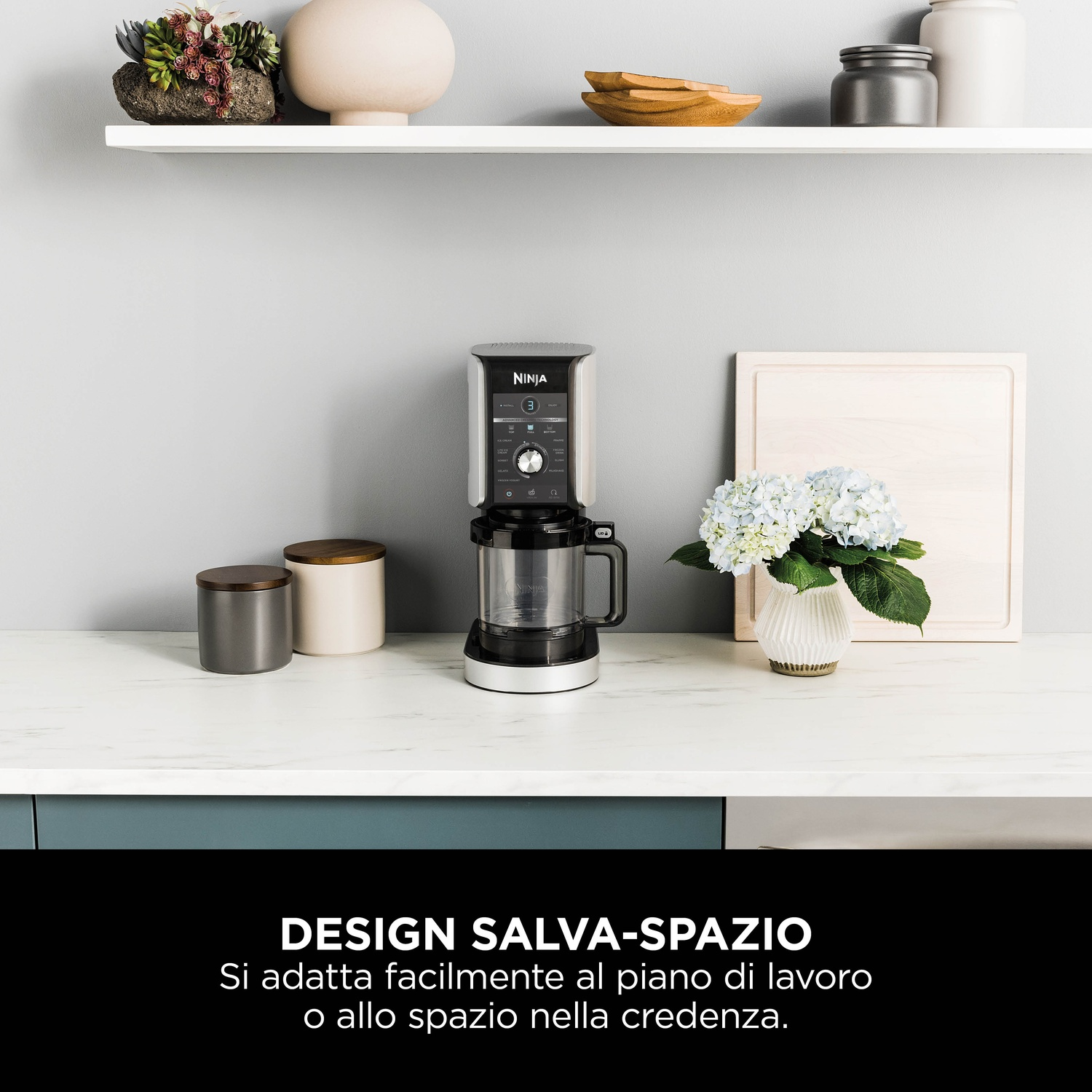 Un elettrodomestico da cucina Ninja è su un piano di lavoro con un vaso di fiori, un tagliere di legno e vari oggetti da cucina.
