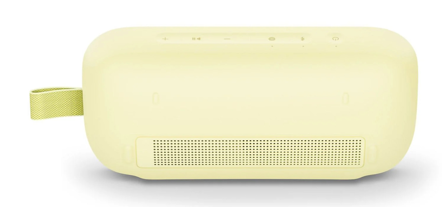 Jasnożółty, zaokrąglony głośnik z przyciskami sterowania na górze i kratką głośnika na dole. Zielona pętla z materiału po lewej stronie.