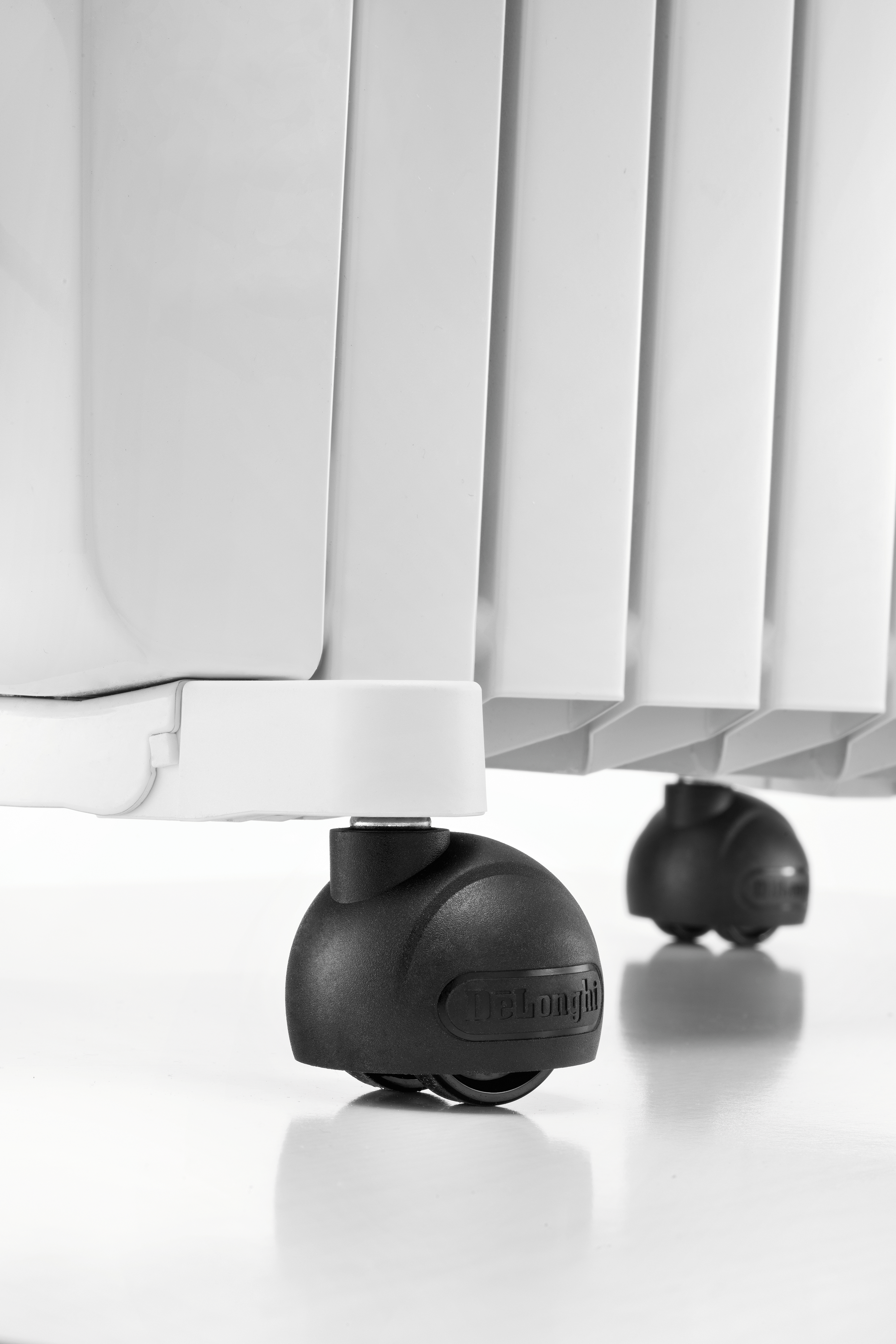 Nahaufnahme eines weißen Heizkörpers mit schwarzen Rädern. Die Räder haben das Delonghi-Logo.