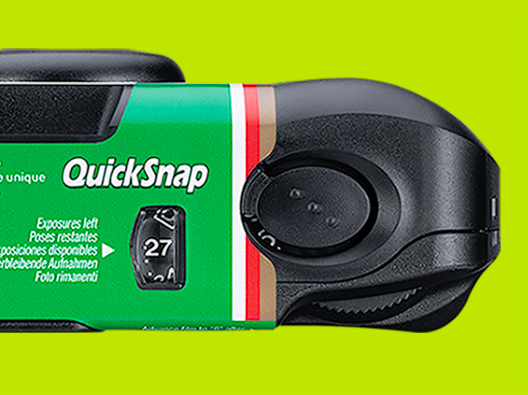 Zbliżenie aparatu QuickSnap. Zielony korpus pokazuje 'QuickSnap' i '27' pozostałych ekspozycji. Widoczne czarne i brązowe detale.