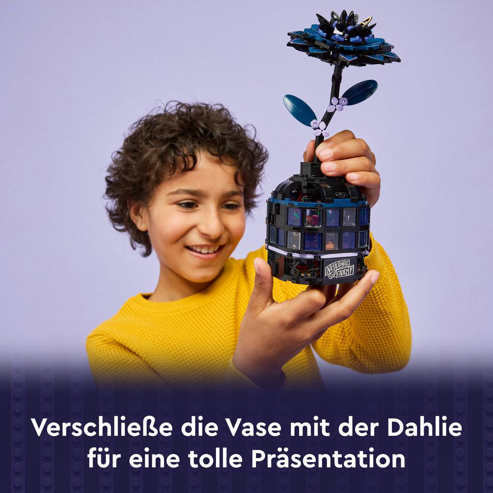 Ein Junge hält ein Lego-Blumenset. Das Set besteht aus einer schwarzen Vase und einer blauen Blume. Der Junge lächelt und trägt ein gelbes Hemd.