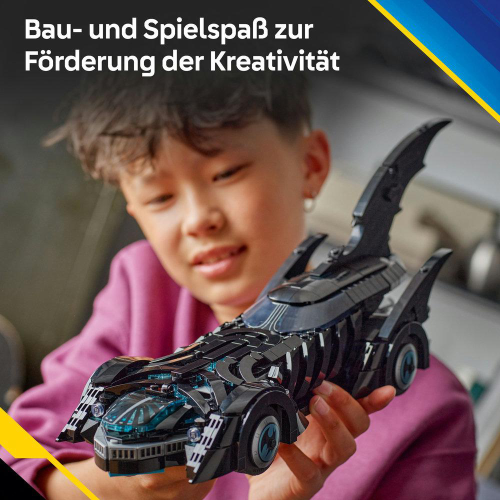 Ein Kind hält ein schwarzes Spielzeugauto. Das Auto hat blaue Akzente und ein markantes Design. Das Kind lächelt, was Freude andeutet.