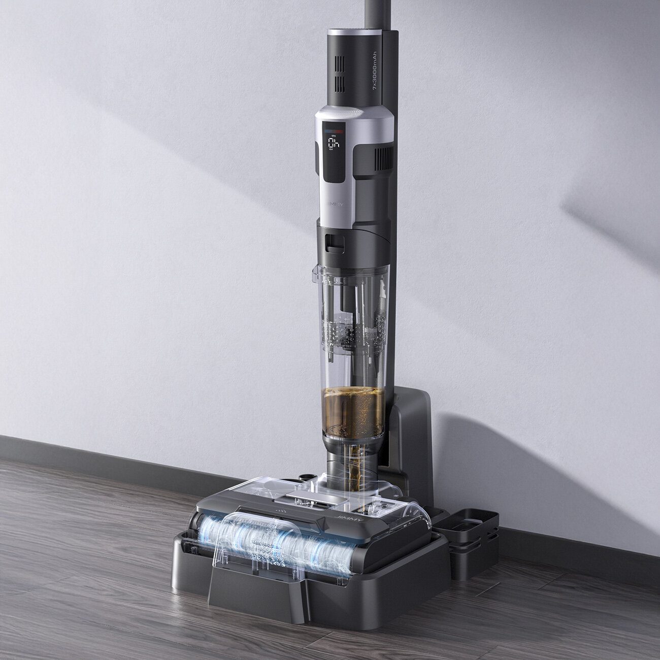 Bezprzewodowy odkurzacz stoi pionowo. Jest czarny i srebrny, z przezroczystym zbiornikiem na wodę. Spoczywa na ciemnoszarej podstawie na drewnianej podłodze.