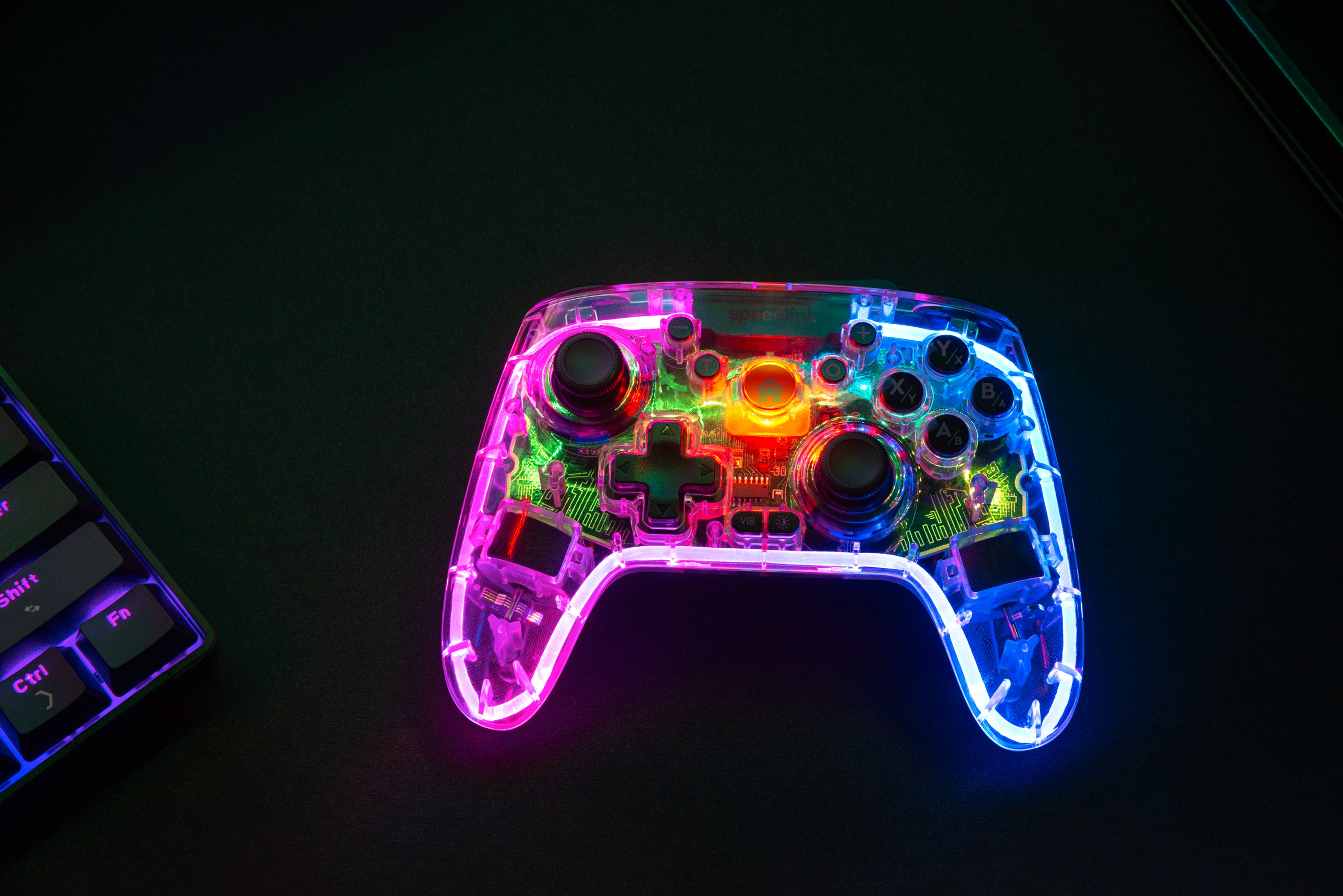 Ein transparentes, beleuchtetes Gamepad auf schwarzem Untergrund. Auf der linken Seite eine Tastatur.