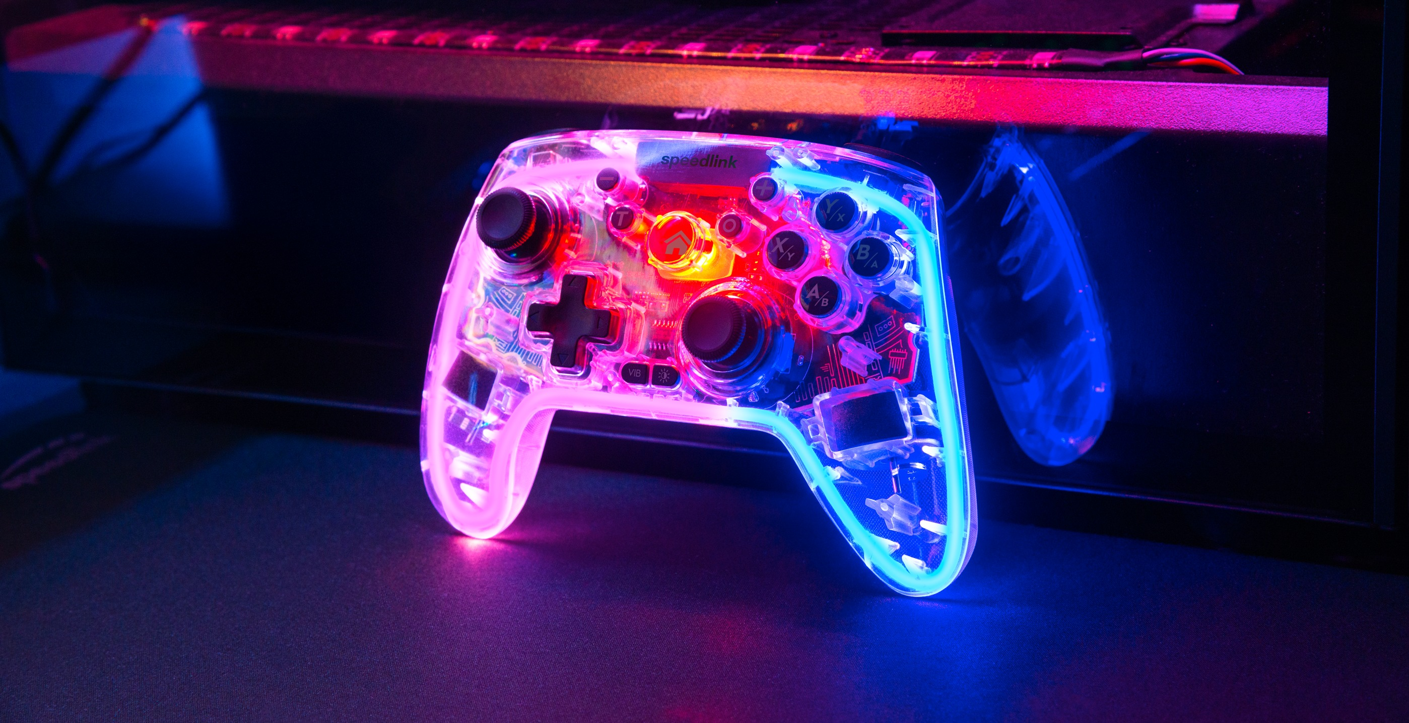 Ein transparentes Speedlink-Spiel-Controller leuchtet mit Neonlichtern. Knöpfe und interne Komponenten sind sichtbar. Hinterleuchtet mit blauem und pinkem Licht.