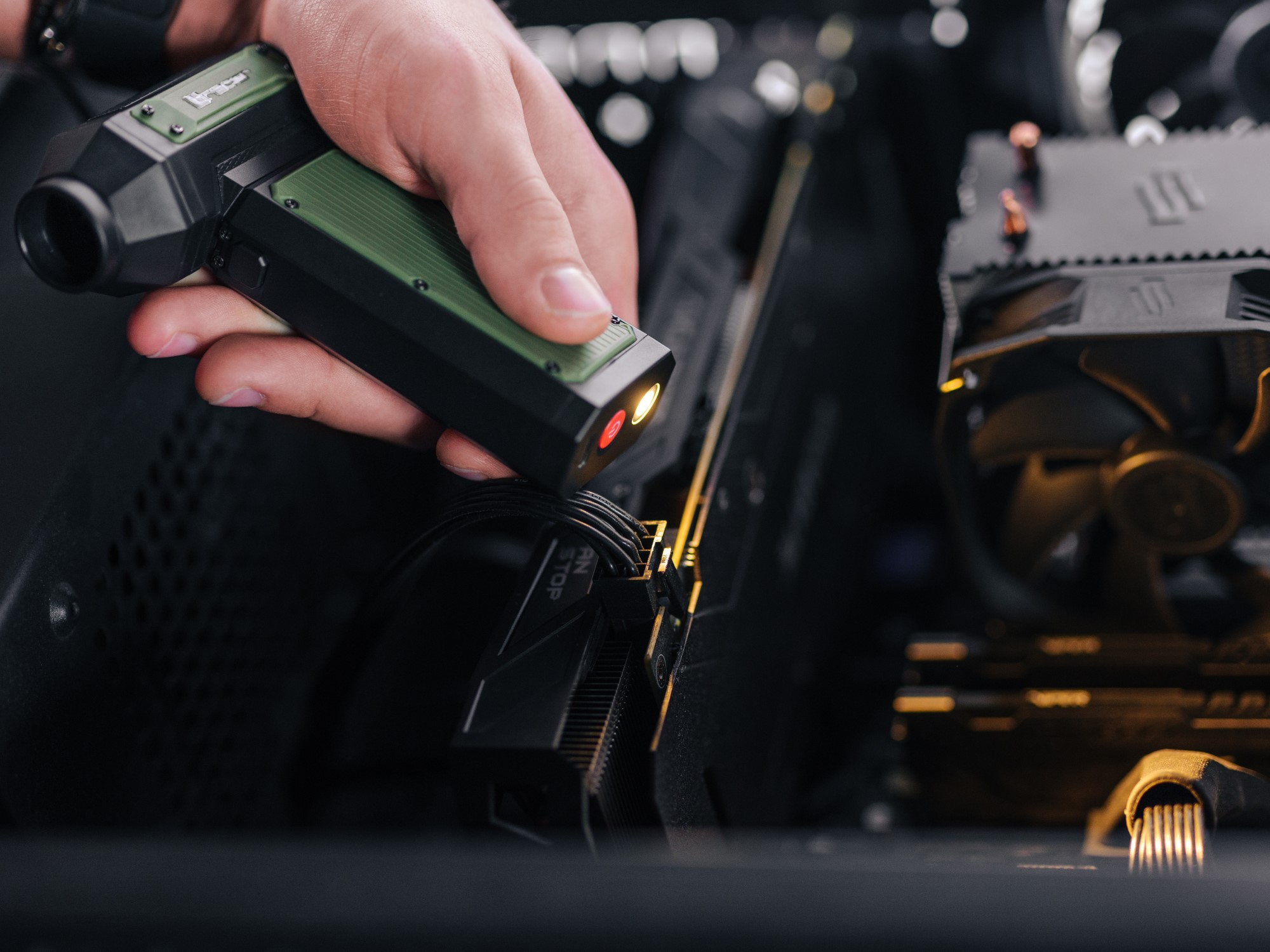 Ręka trzyma czarno-zielone urządzenie, oświetlając komponent komputera. Scena rozgrywa się w obudowie komputera.