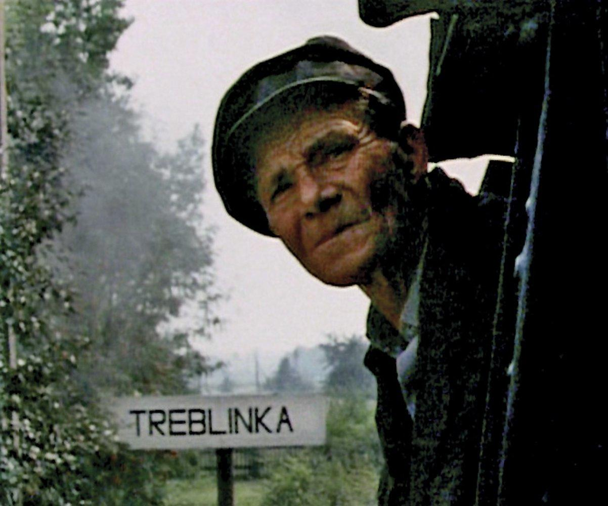 Ein Mann mit Mütze schaut heraus. Ein Schild liest Treblinka. Bäume und ein nebliger Hintergrund.