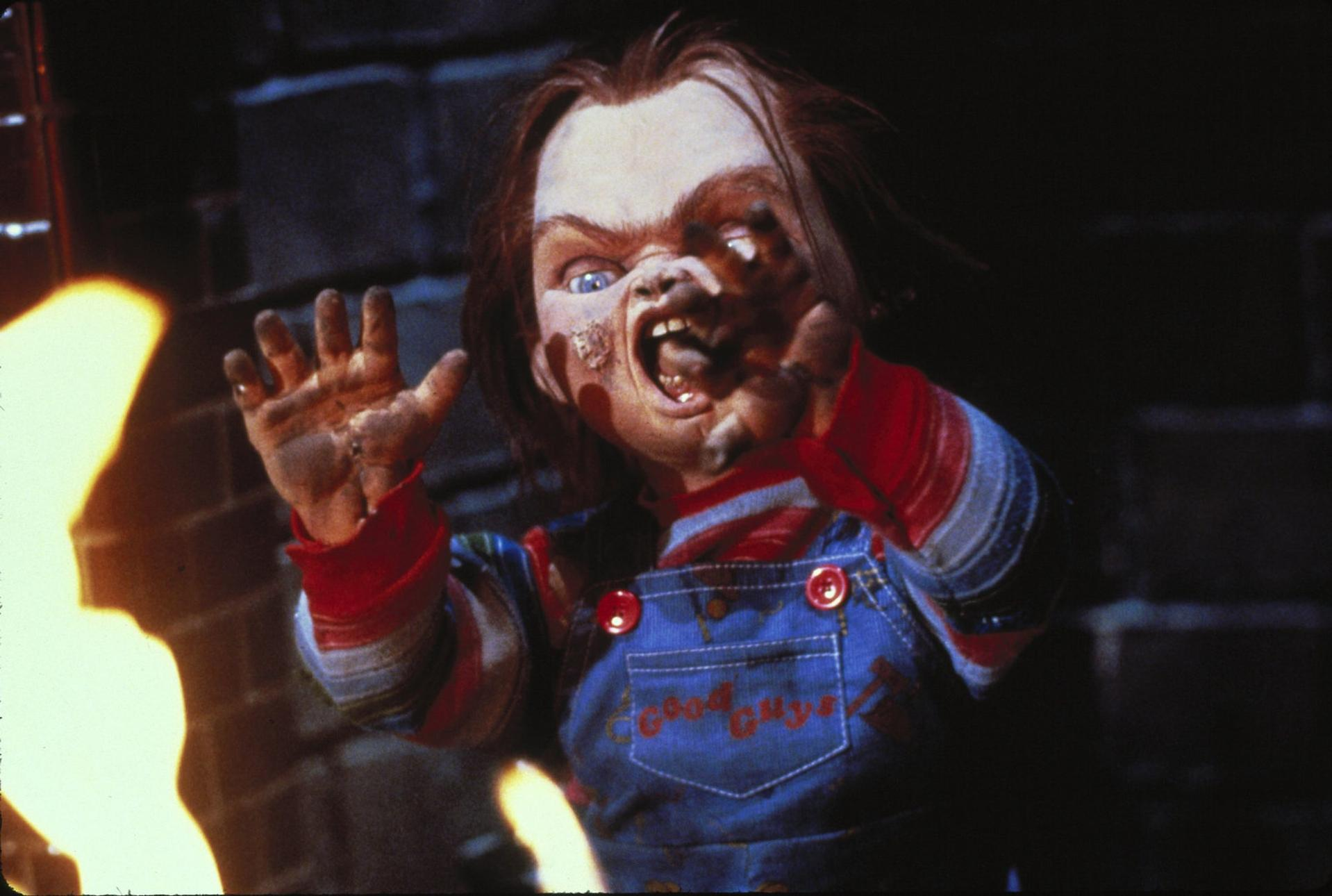 Chucky-Puppe mit bedrohlichem Ausdruck. Sie trägt blaue Latzhosen, rote und gestreifte Ärmel und einen weit geöffneten Mund.