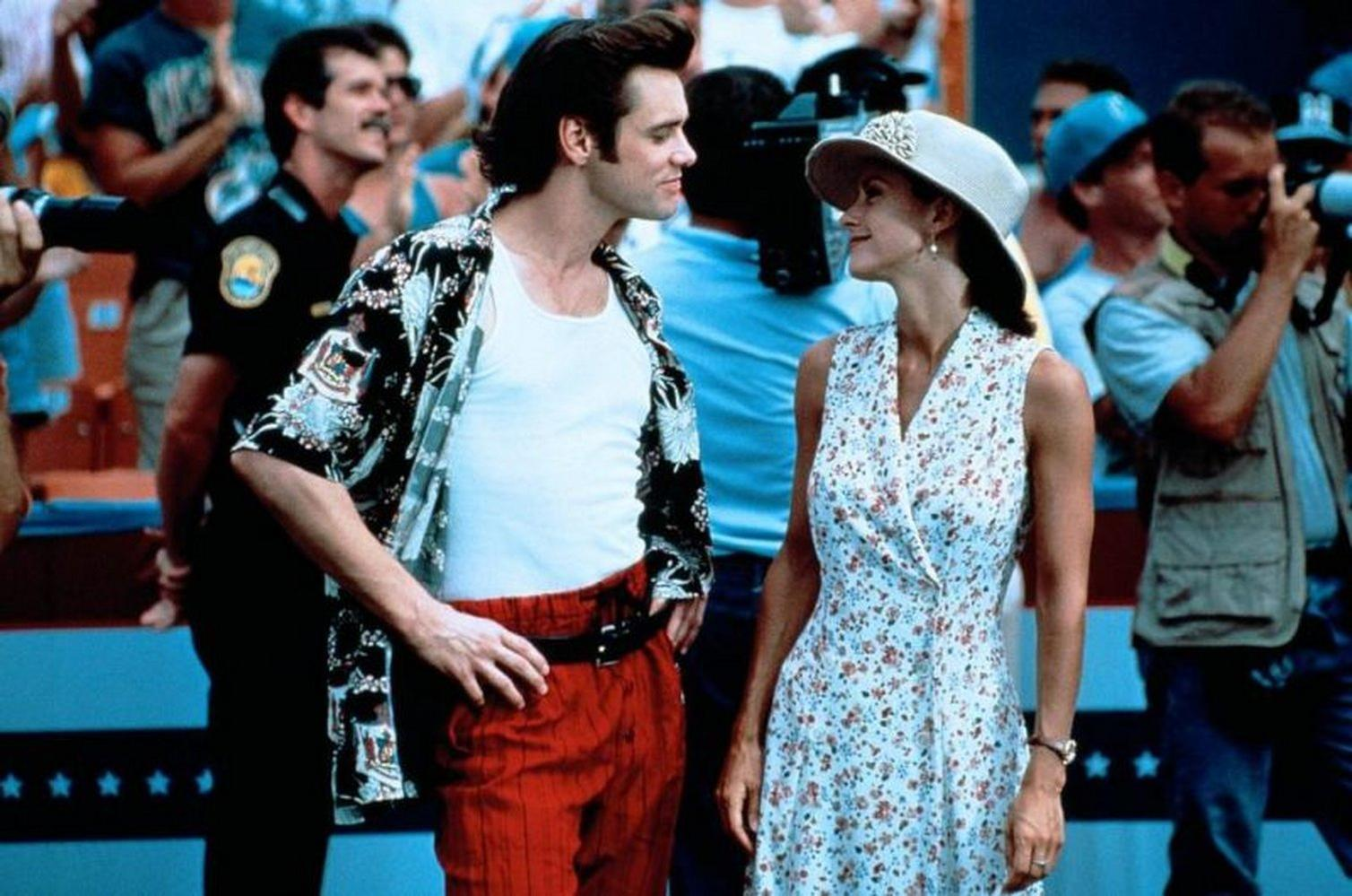 Jim Carrey und eine Frau stehen sich gegenüber, umgeben von einer Menschenmenge. Carrey trägt ein Hawaiihemd und eine rote Hose.