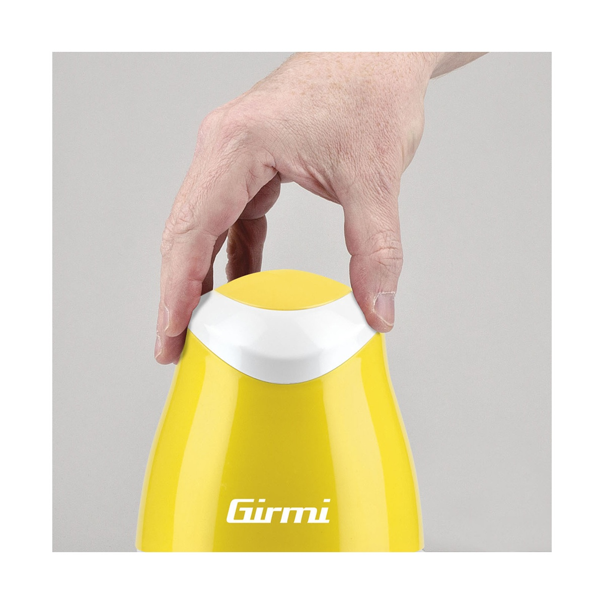 Una mano tiene in mano un elettrodomestico Girmi giallo e bianco. Lo sfondo è grigio chiaro.