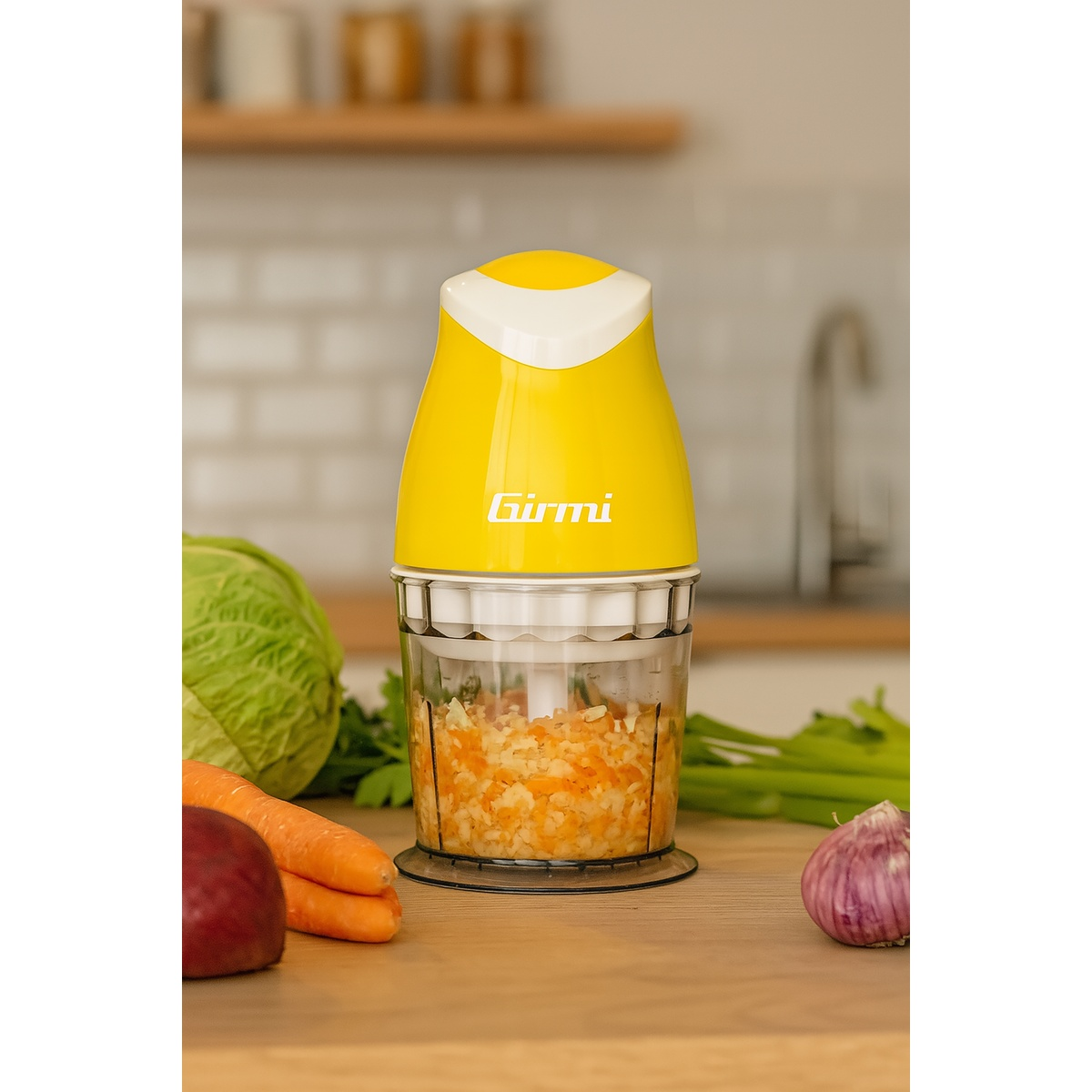 Un tritatutto Girmi giallo con verdure tritate all'interno. Carote, cavolo e aglio sono sul tavolo di legno.