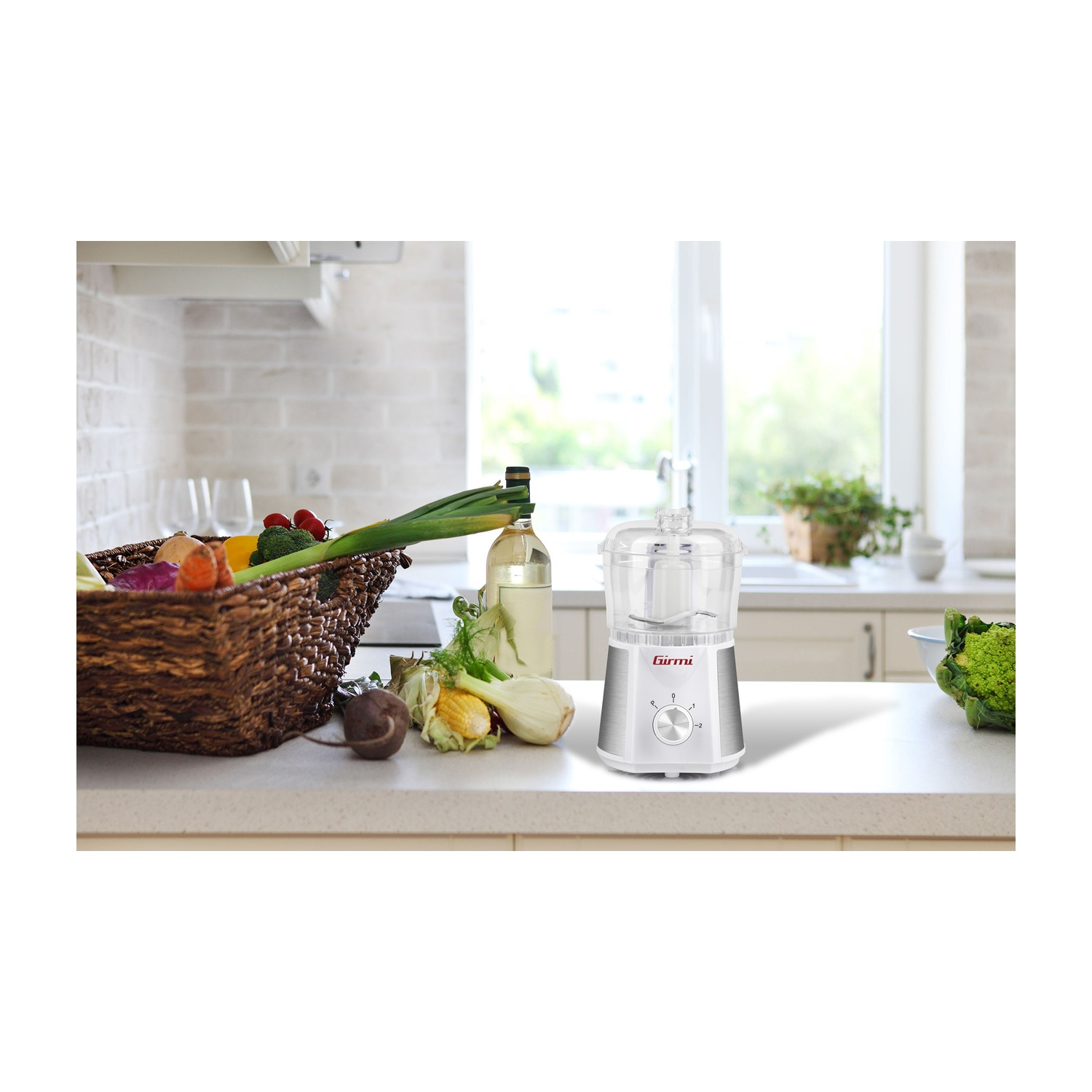 Scena di cucina con robot da cucina, cestino di verdure e bottiglia d'olio sul piano. Luce naturale.