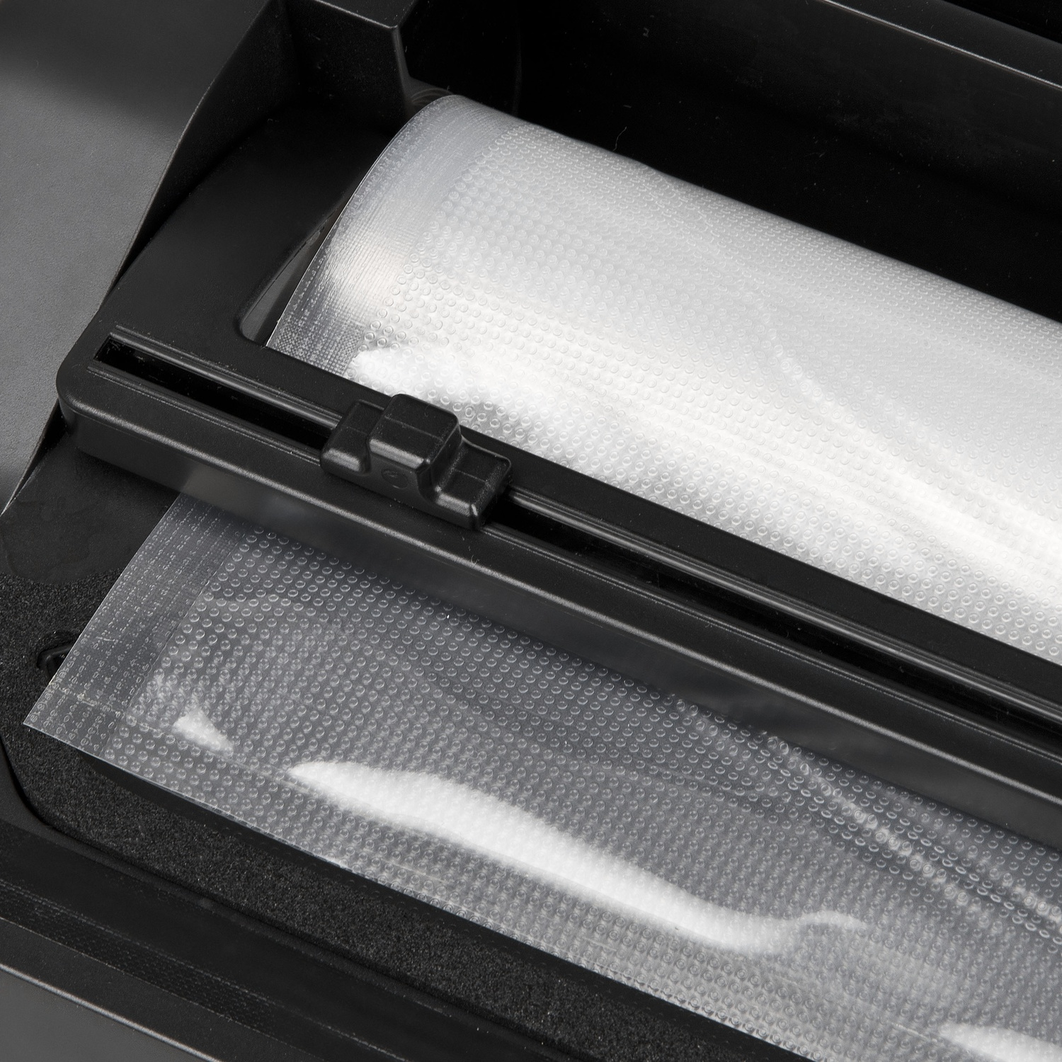 Primo piano di una sigillatrice per alimenti nera con un rotolo di plastica trasparente e un sacchetto di plastica sigillato. La plastica ha un motivo a bolle.