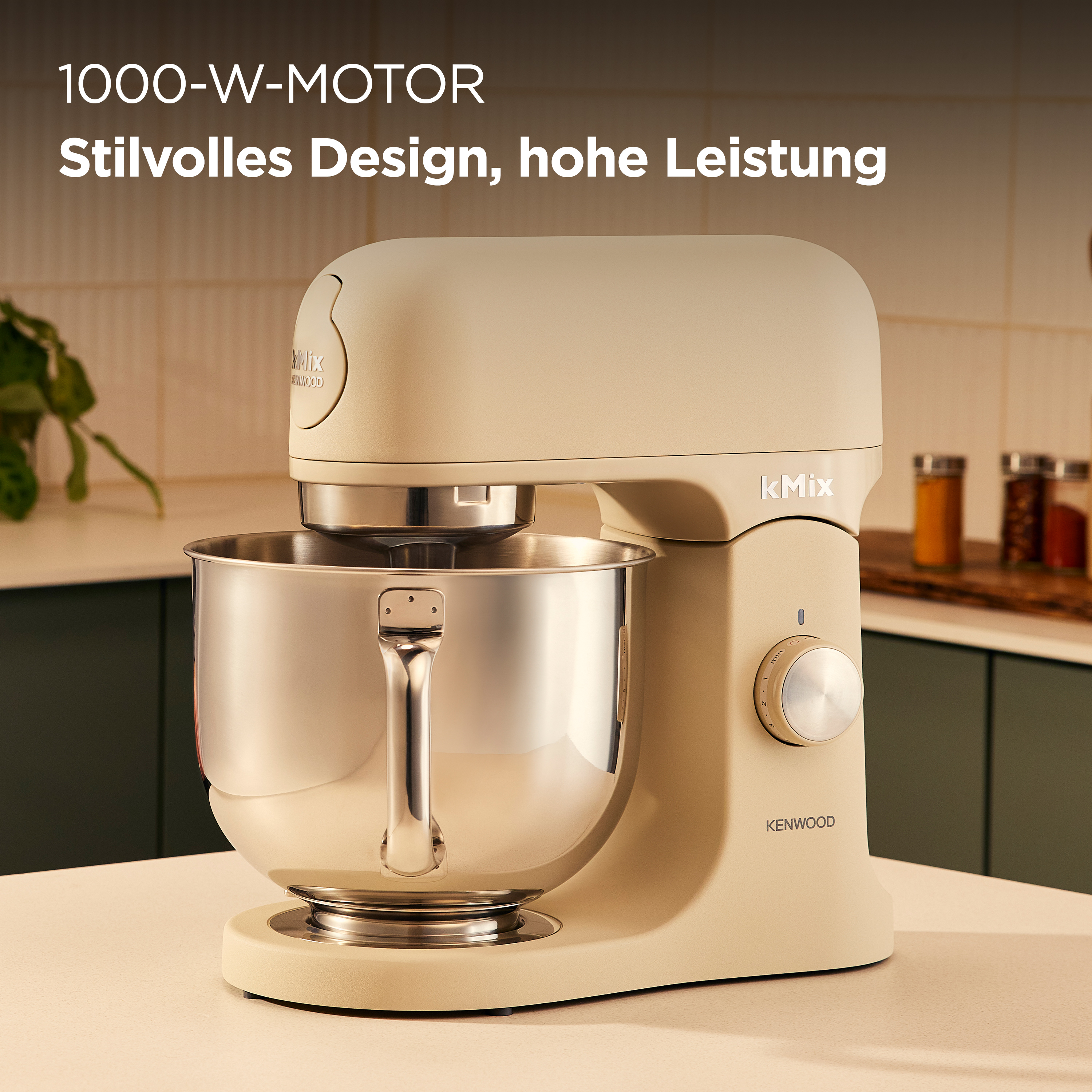 Ein cremefarbener Kmix-Küchenmixer mit einer Edelstahlschüssel auf einer hellen Oberfläche. Hintergrund hat Gewürzgläser.