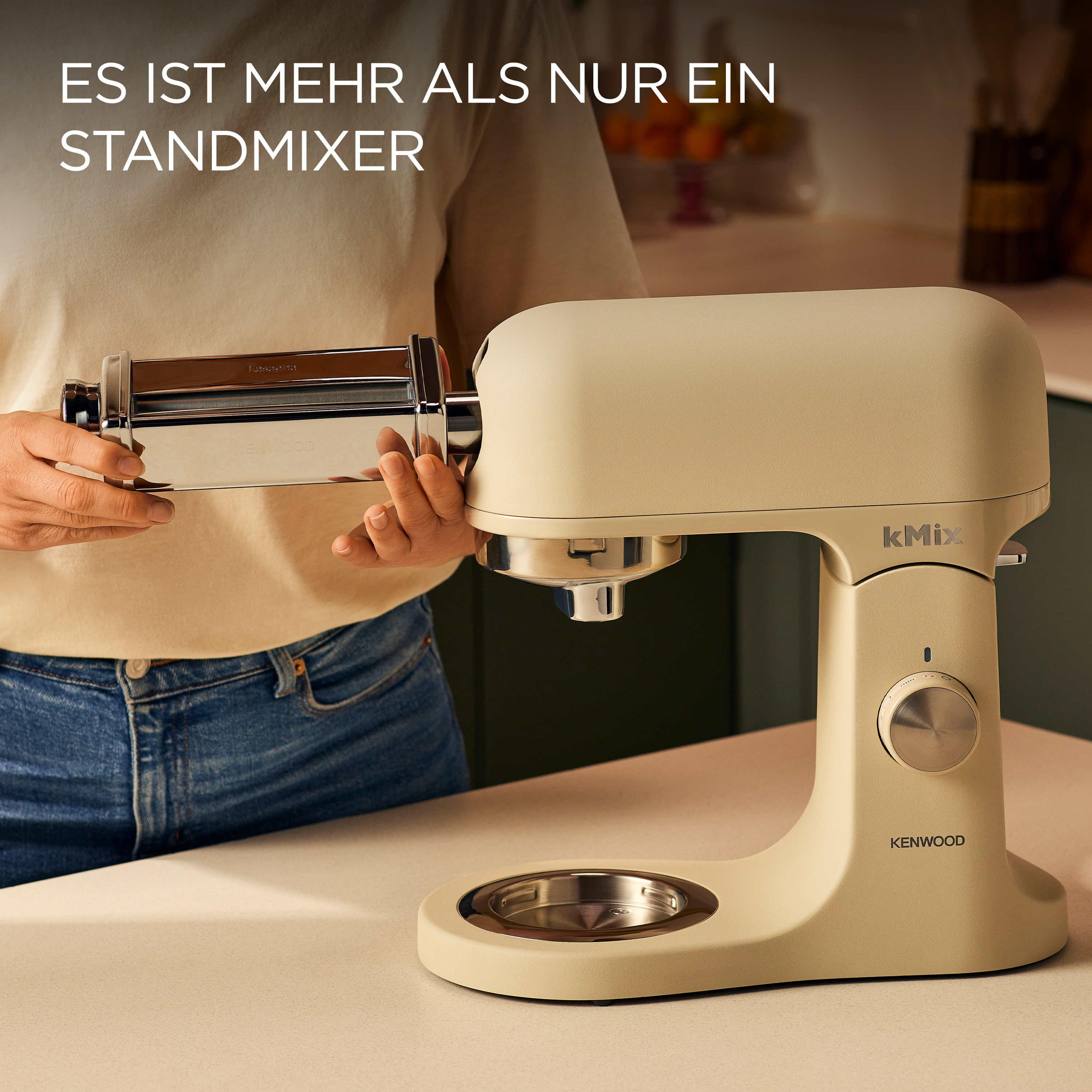 Eine Person hält einen Pastamacher-Aufsatz für einen beigefarbenen Kenwood-Küchenmixer. Küchenszene mit Text auf Deutsch.