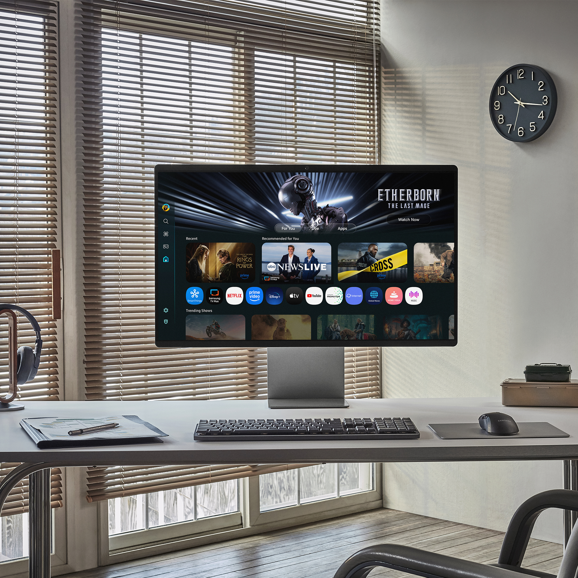 Ein Monitor zeigt einen Streaming-Dienst. Jalousien bedecken das Fenster. Eine Uhr hängt an der Wand. Tastatur und Maus sind sichtbar.
