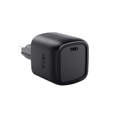 Egy fekete Trust USB-C töltő fekete háttérrel. Van rajta egy dugó és a Trust logója az oldalán.